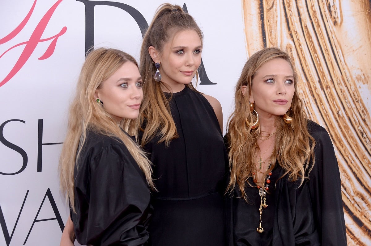 Elizabeth Olsen standing in the center of Mary-Kate and Ashley Olsen with all of them dressed in black