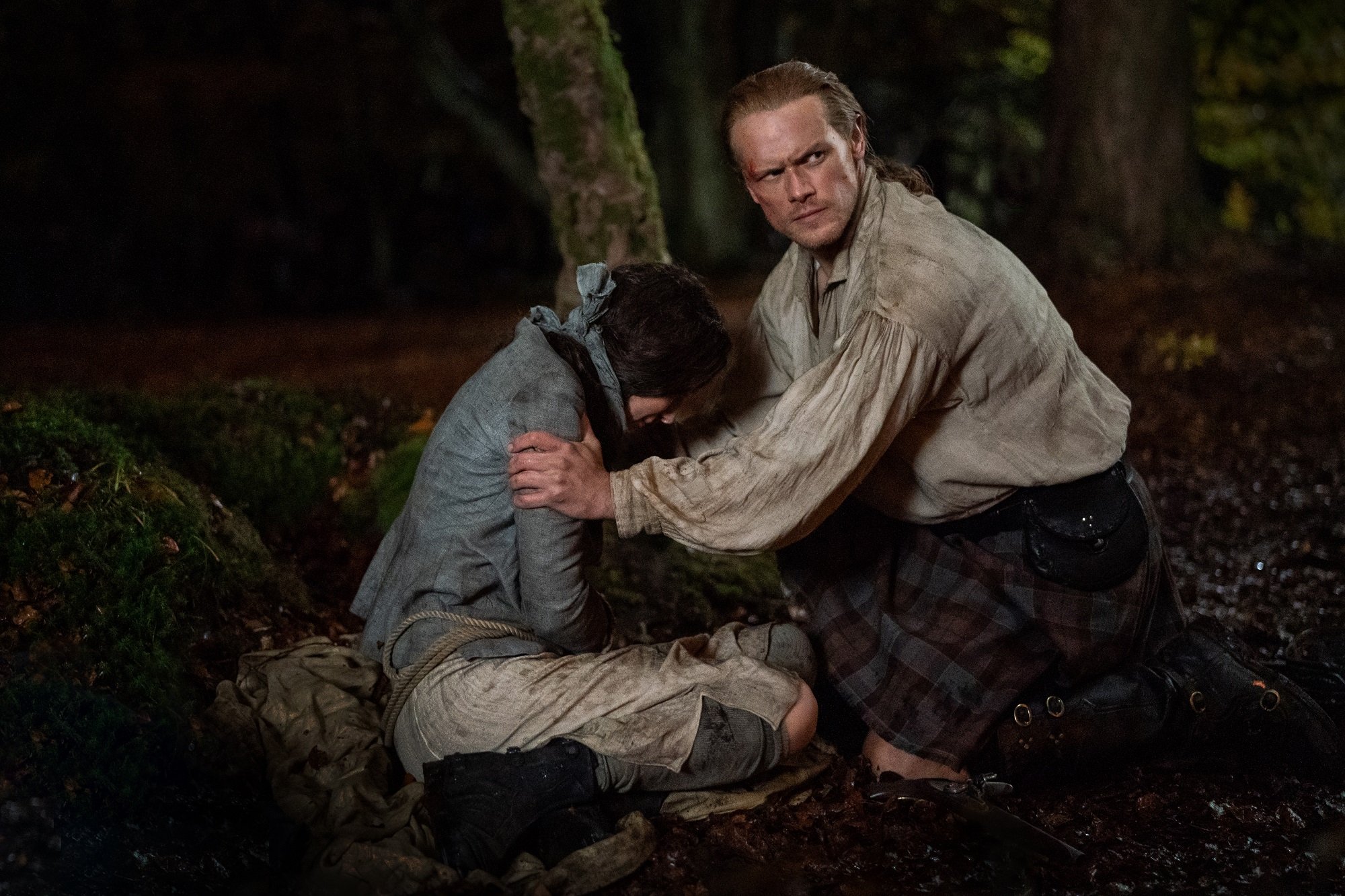 Outlander: Sam Heughan kneels with an injured comrade