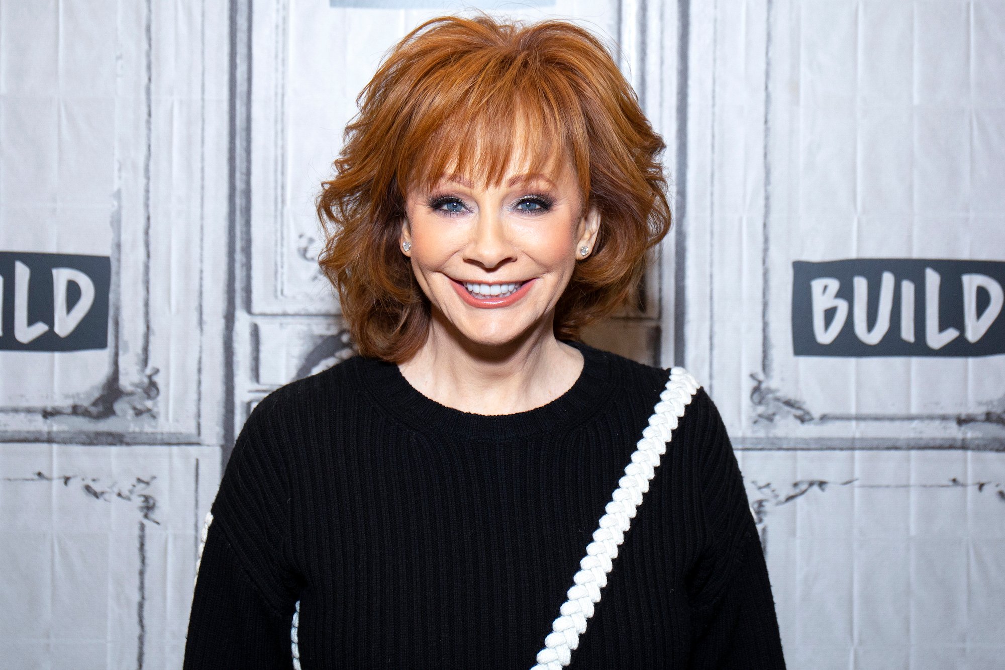 Reba McEntire smiling in front of a white background