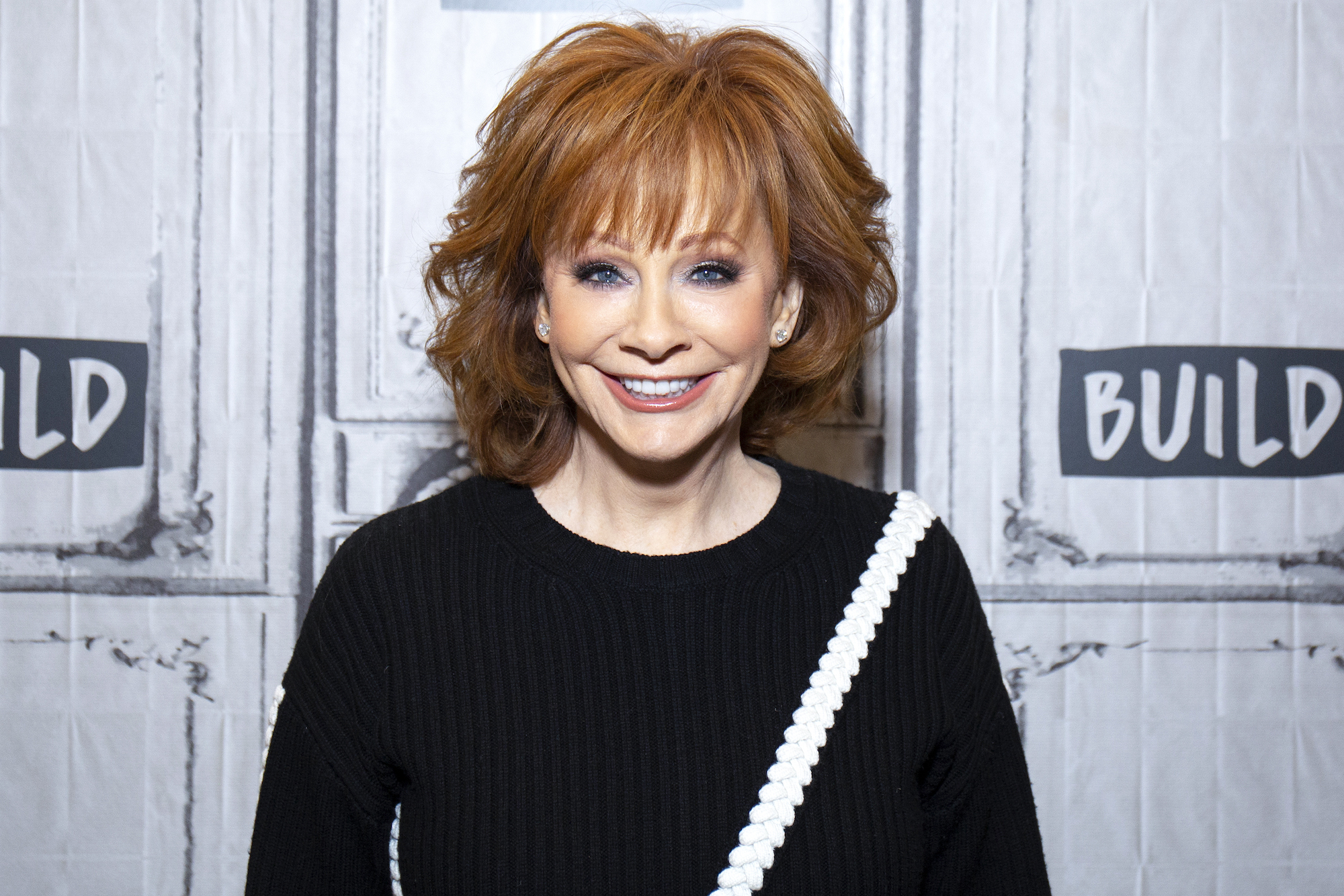 Reba McEntire smiling in front of a white background