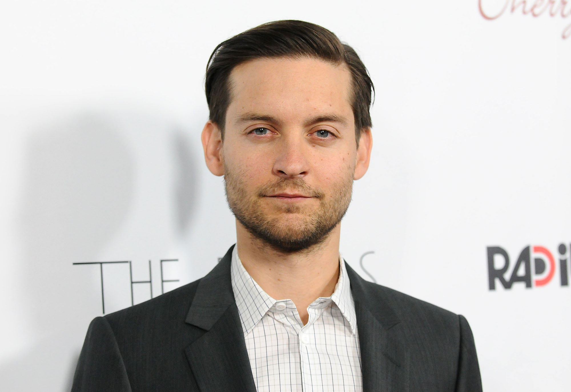 Tobey Maguire smiling in front of a white background