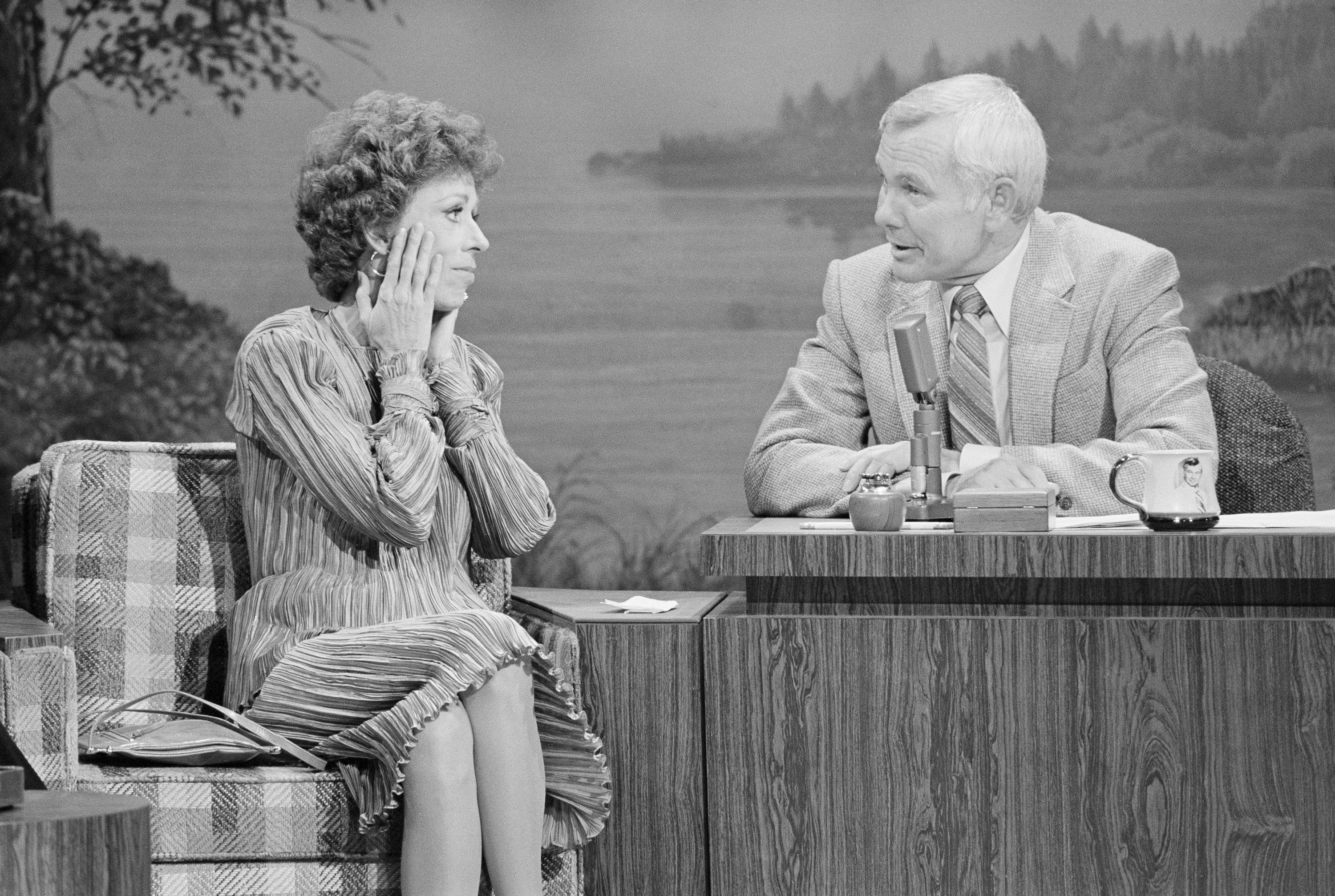 Carol Burnett near Johnny Carson at his desk