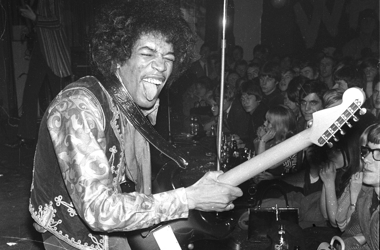 Hendrix sticks out his tongue while playing guitar on his knees 