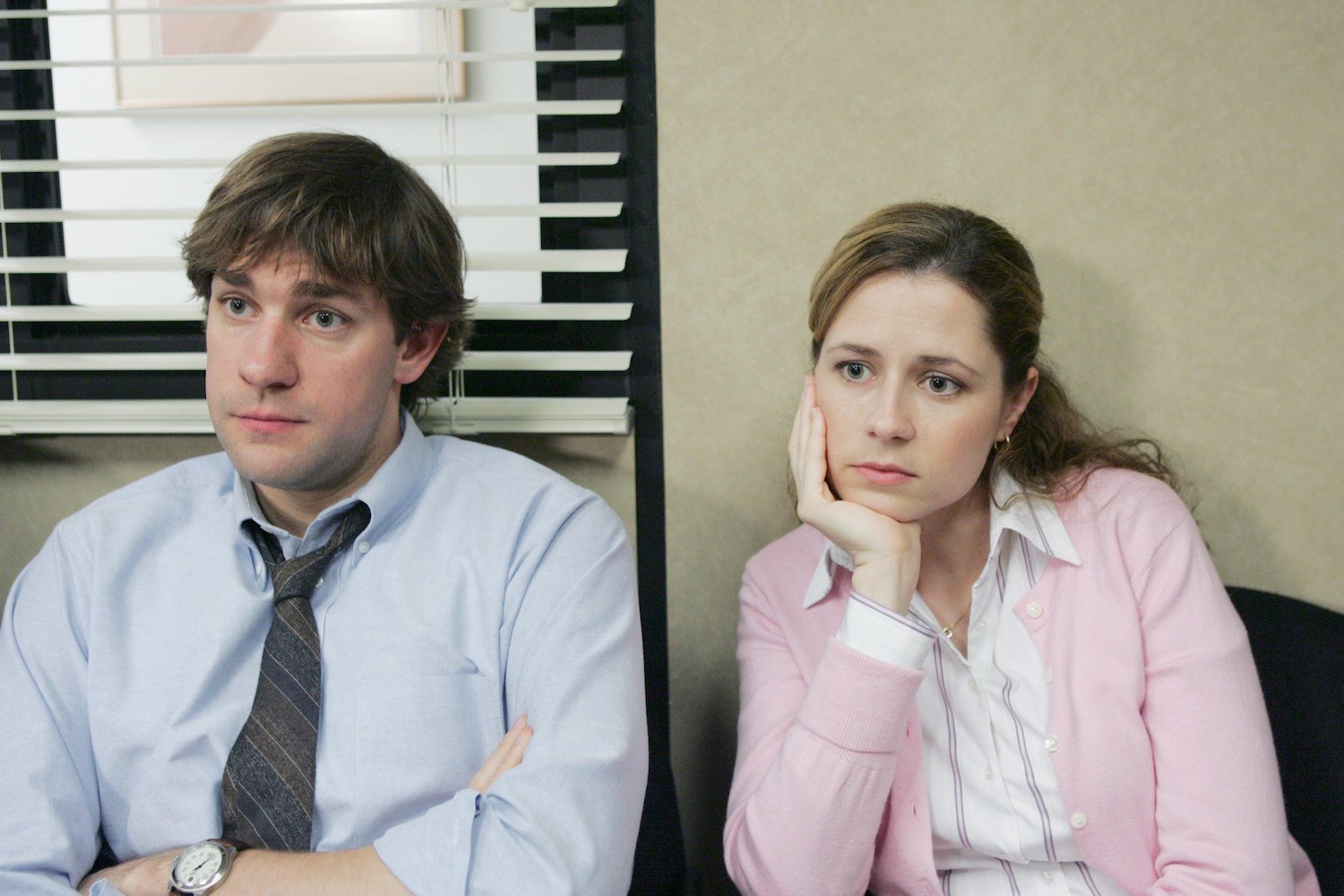 The Office stars John Krasinski as Jim Halpert and Jenna Fischer as Pam Beesly sit next to each other in the conference room