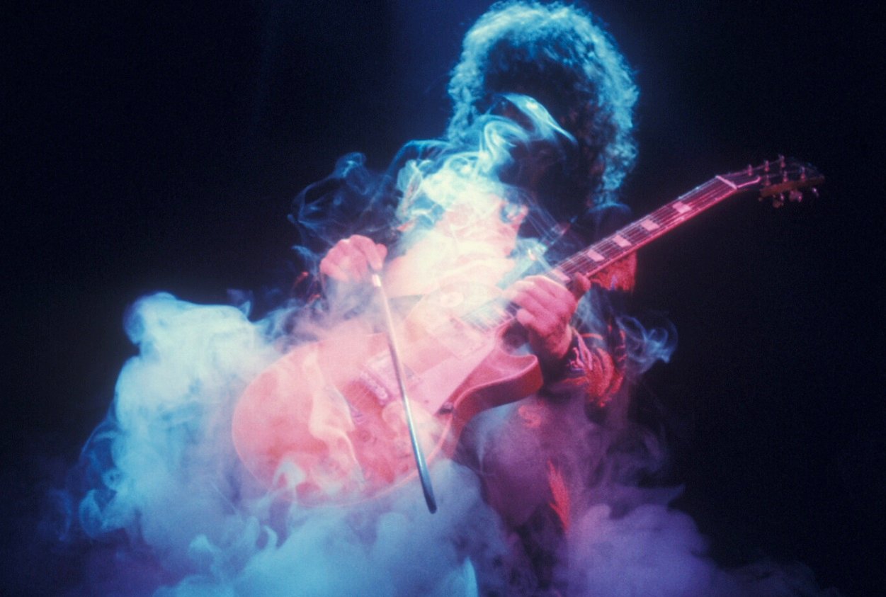 Jimmy Page obscured by smoke while playing guitar on stage in 1975