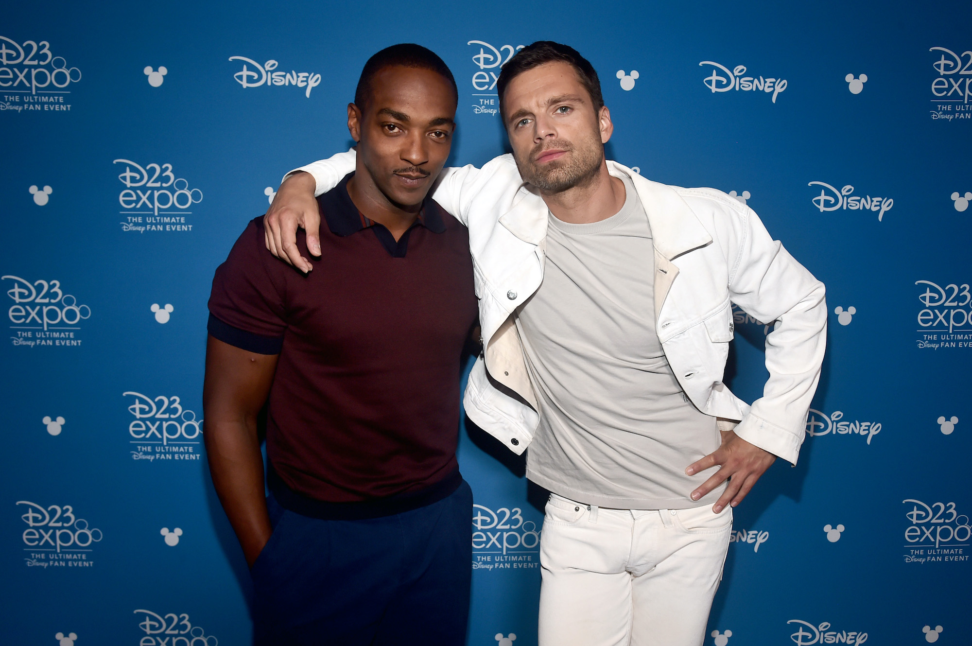 (L-R) Anthony Mackie and Sebastian Stan in front of a blue background with repeating logos