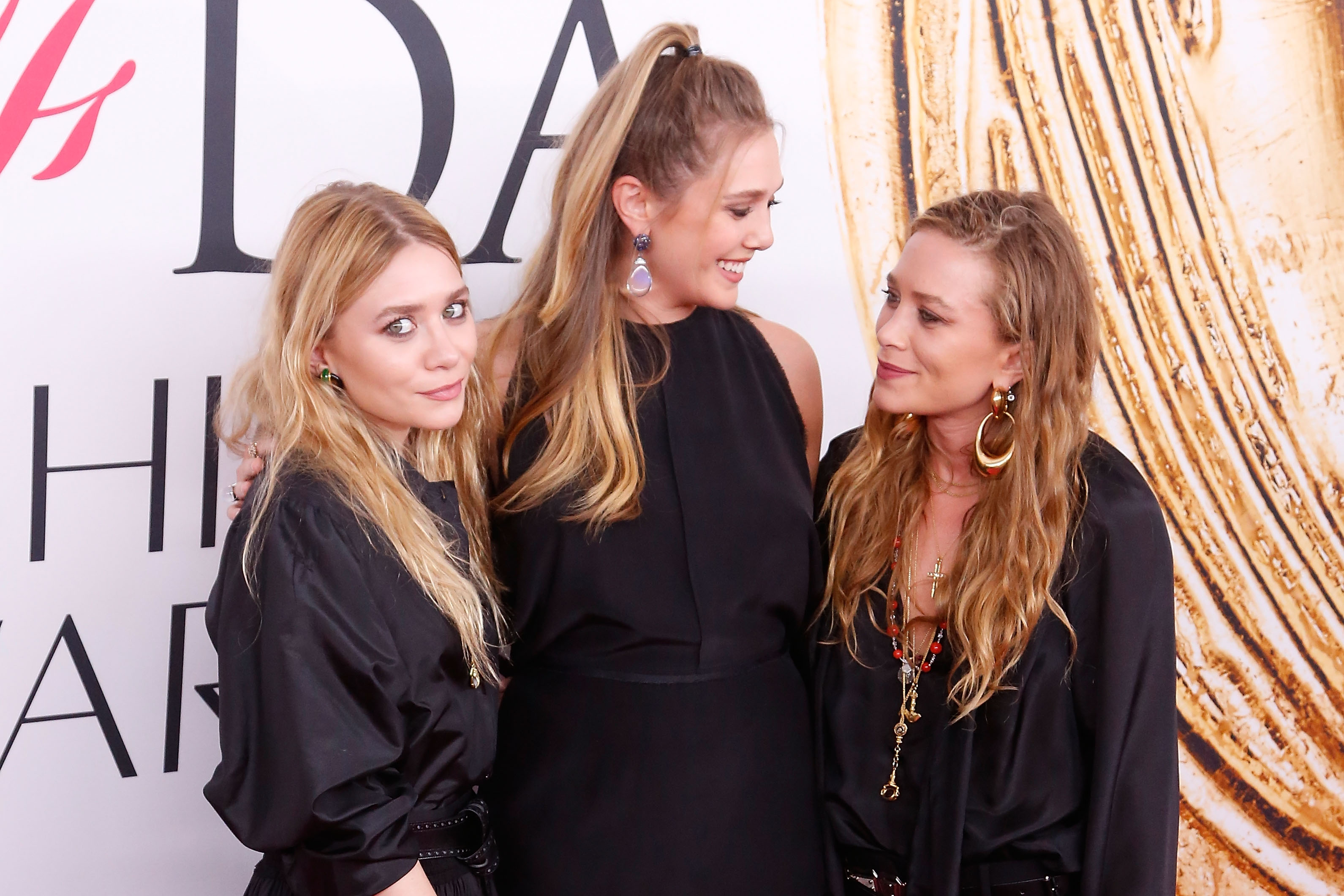 Ashley Olsen, Elizabeth Olsen, and Mary-Kate Olsen smiling in all black at an event.