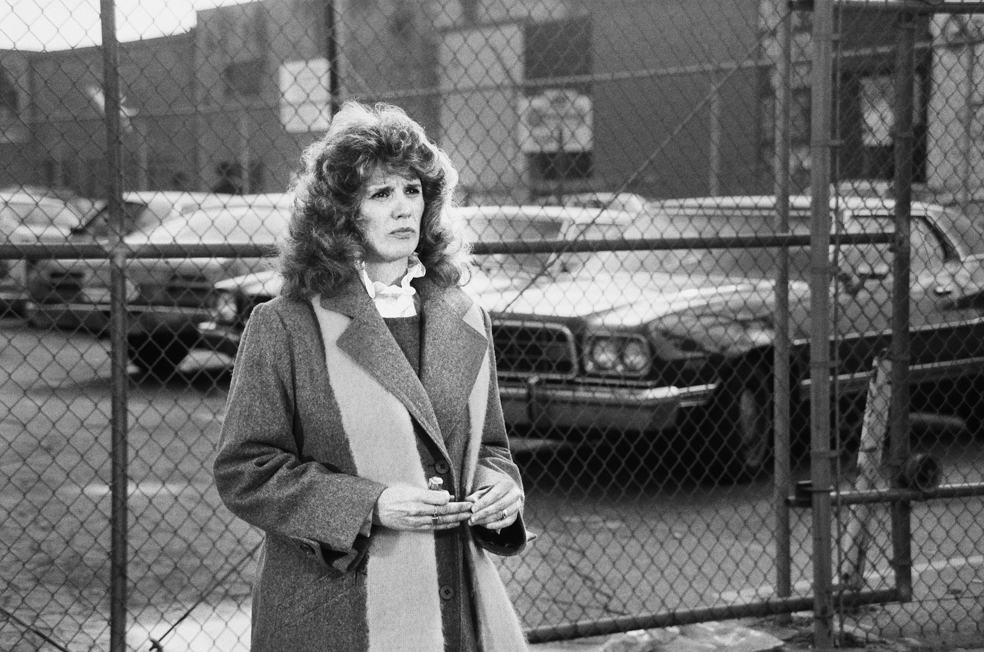Barbara Bosson on 'Hill Street Blues' standing in front of a fenced in parking lot, in black and white
