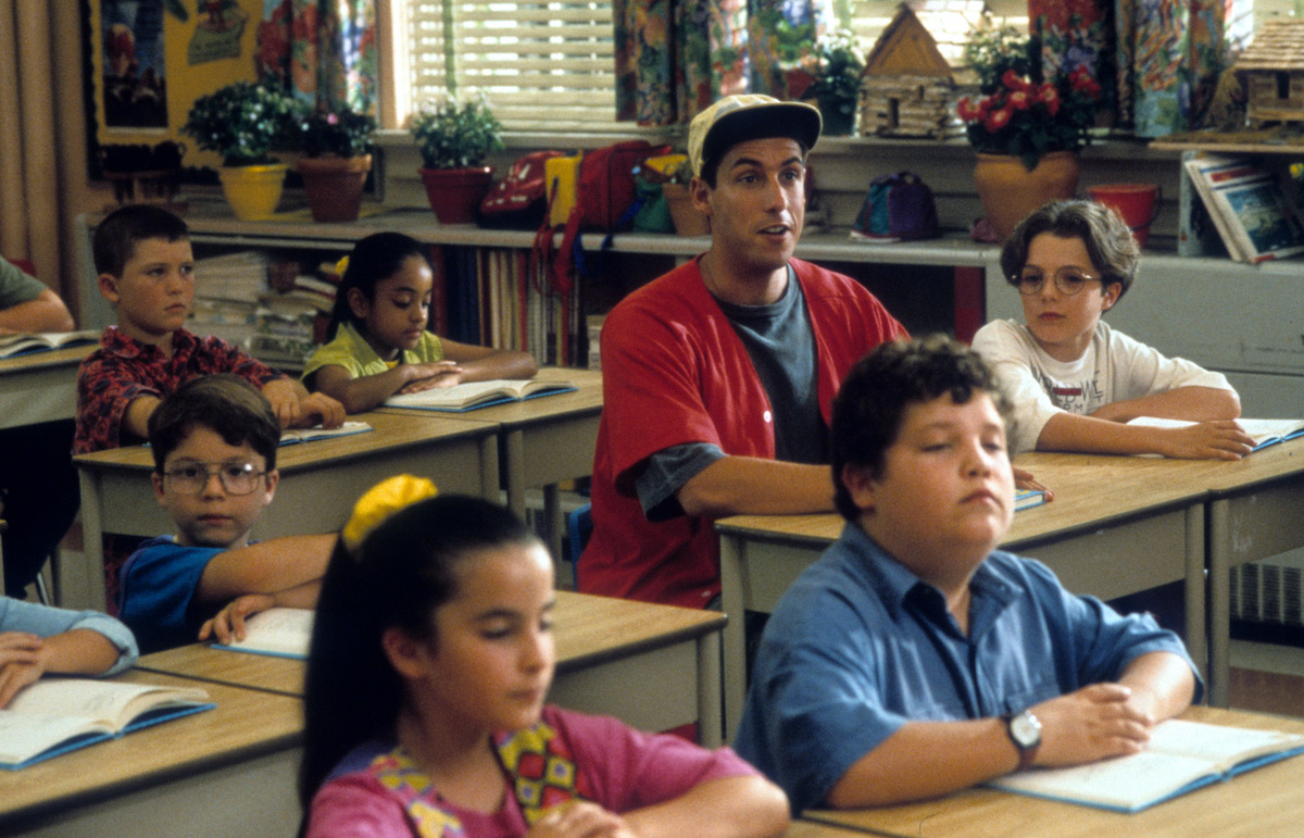 Adam Sandler sitting at a desk in a class for children in a scene from the film 'Billy Madison'