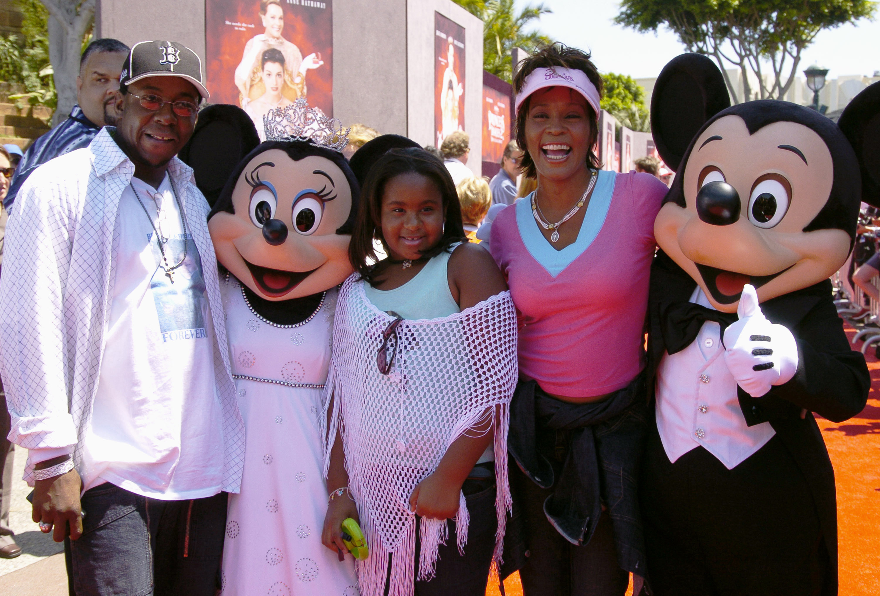 Bobby Brown, Bobbi Kristina Brown, and Whitney Houston smiling at DisneyLand resort.