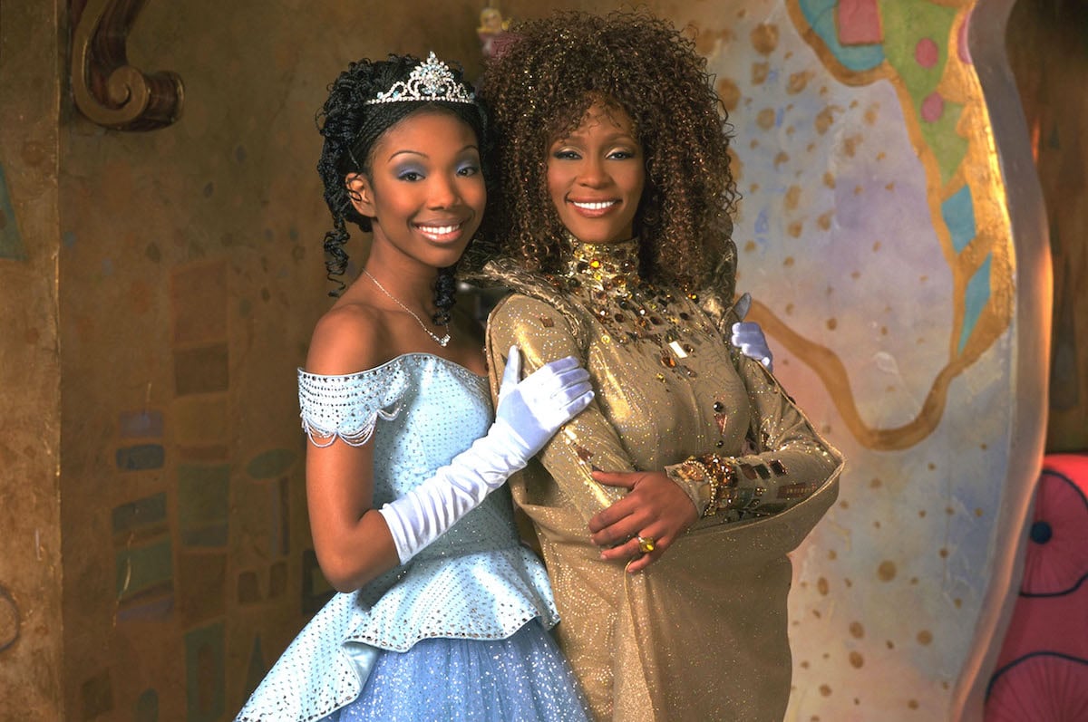 Brandy Norwood in a blue ballgown and Whitney Houston in a gold gown pose side-by-side and smile in a press image for 'Rodgers and Hammerstein's Cinderella' on ABC, 1997 | Disney
