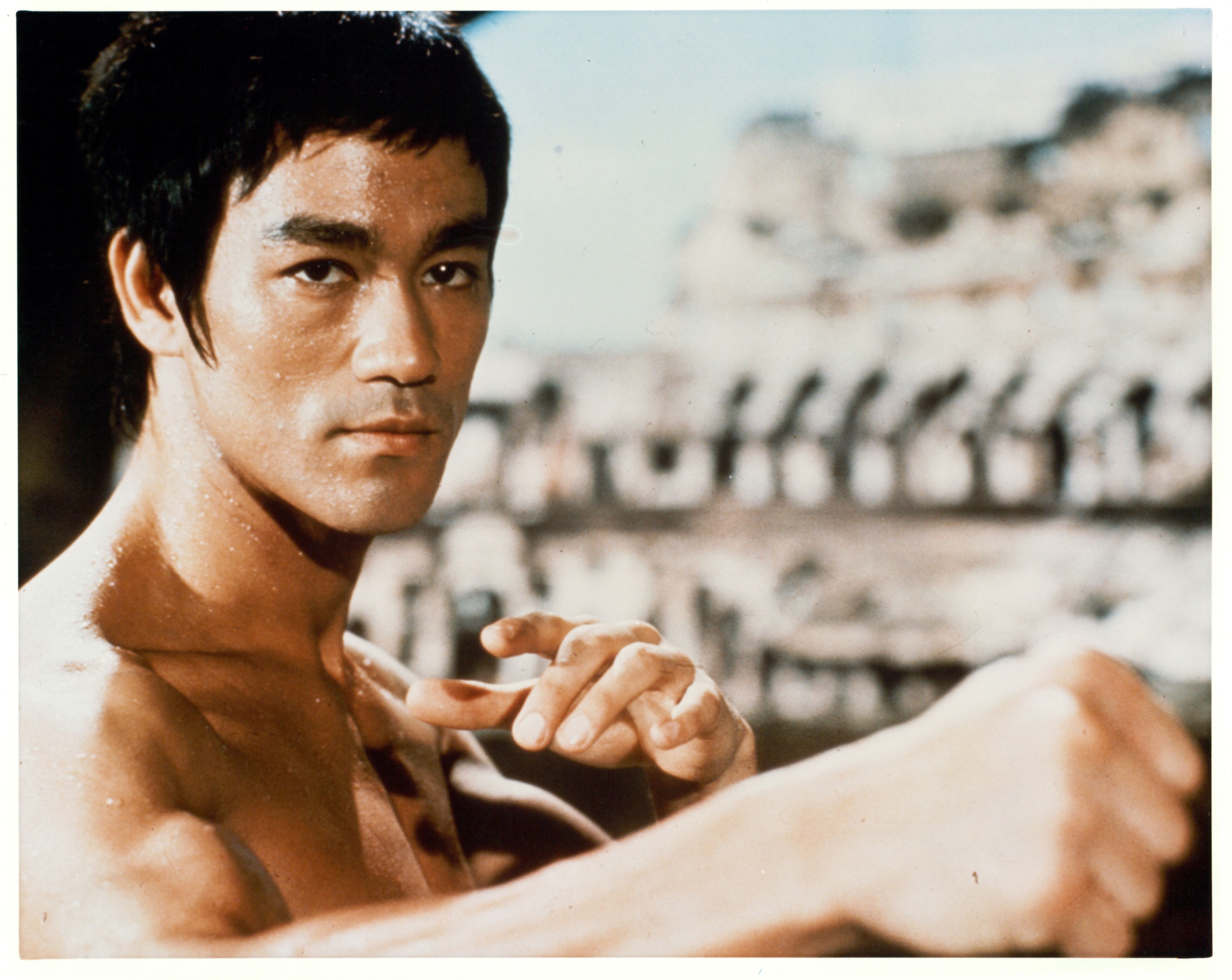 Bruce Lee looking away from the camera, shirtless, with his arms slightly outstretched
