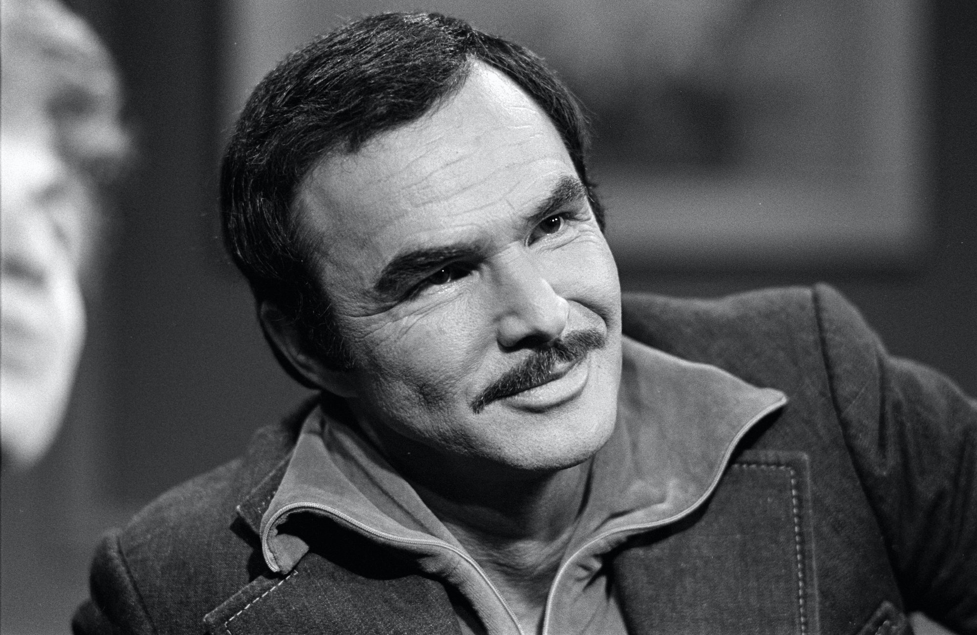Burt Reynolds smiling, head tilted, in black and white