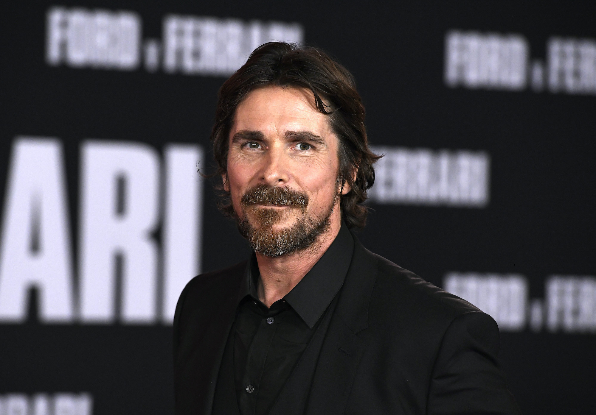 Christian Bale smiling in front of a blurred black and white background