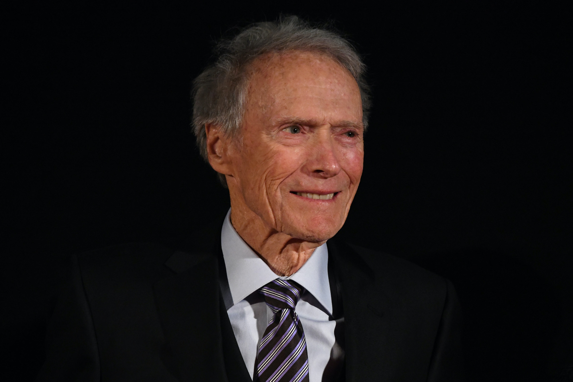 Clint Eastwood smiling in front of a black background