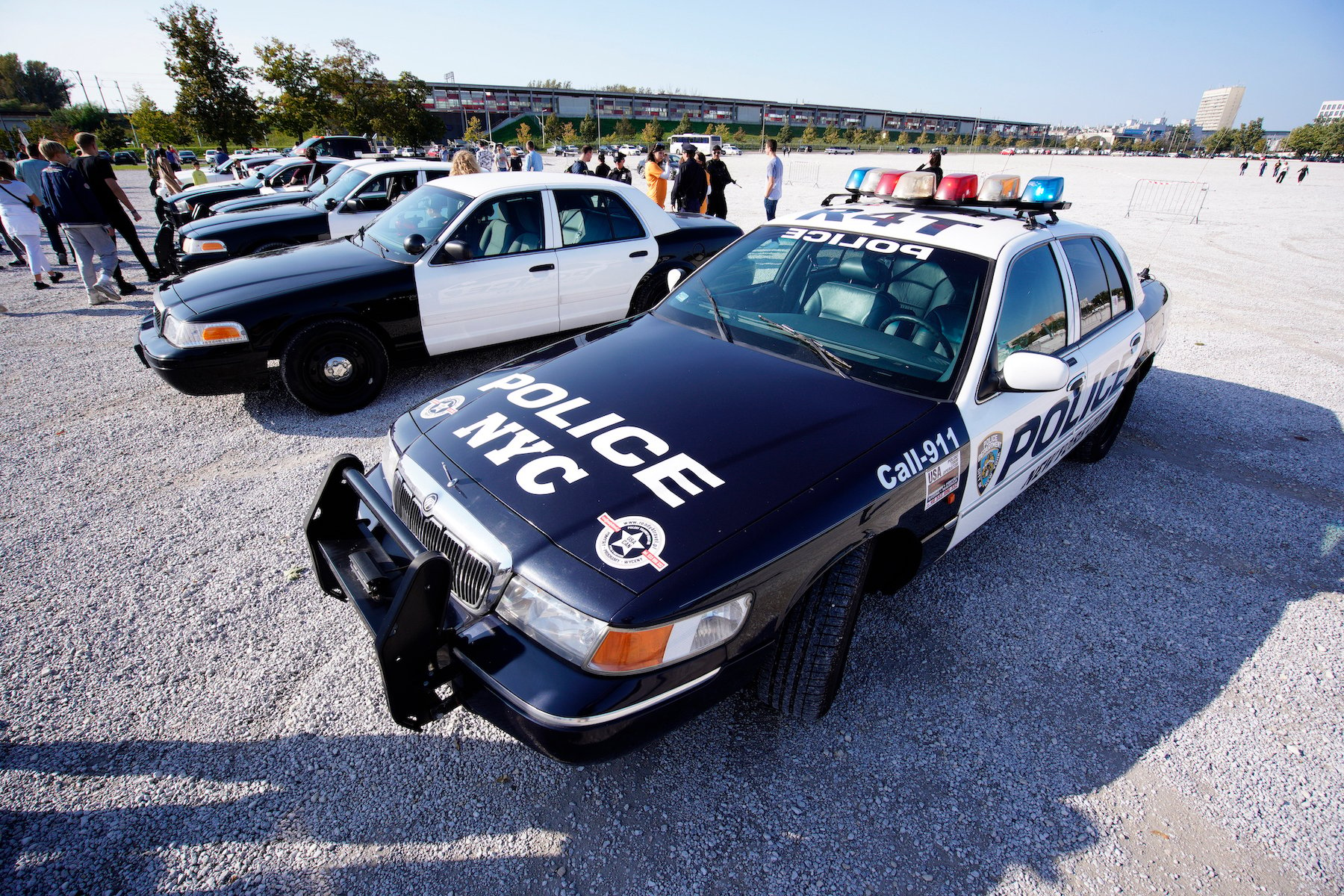 American police car with lights in front with other American police cars in the distance, in a parking lot