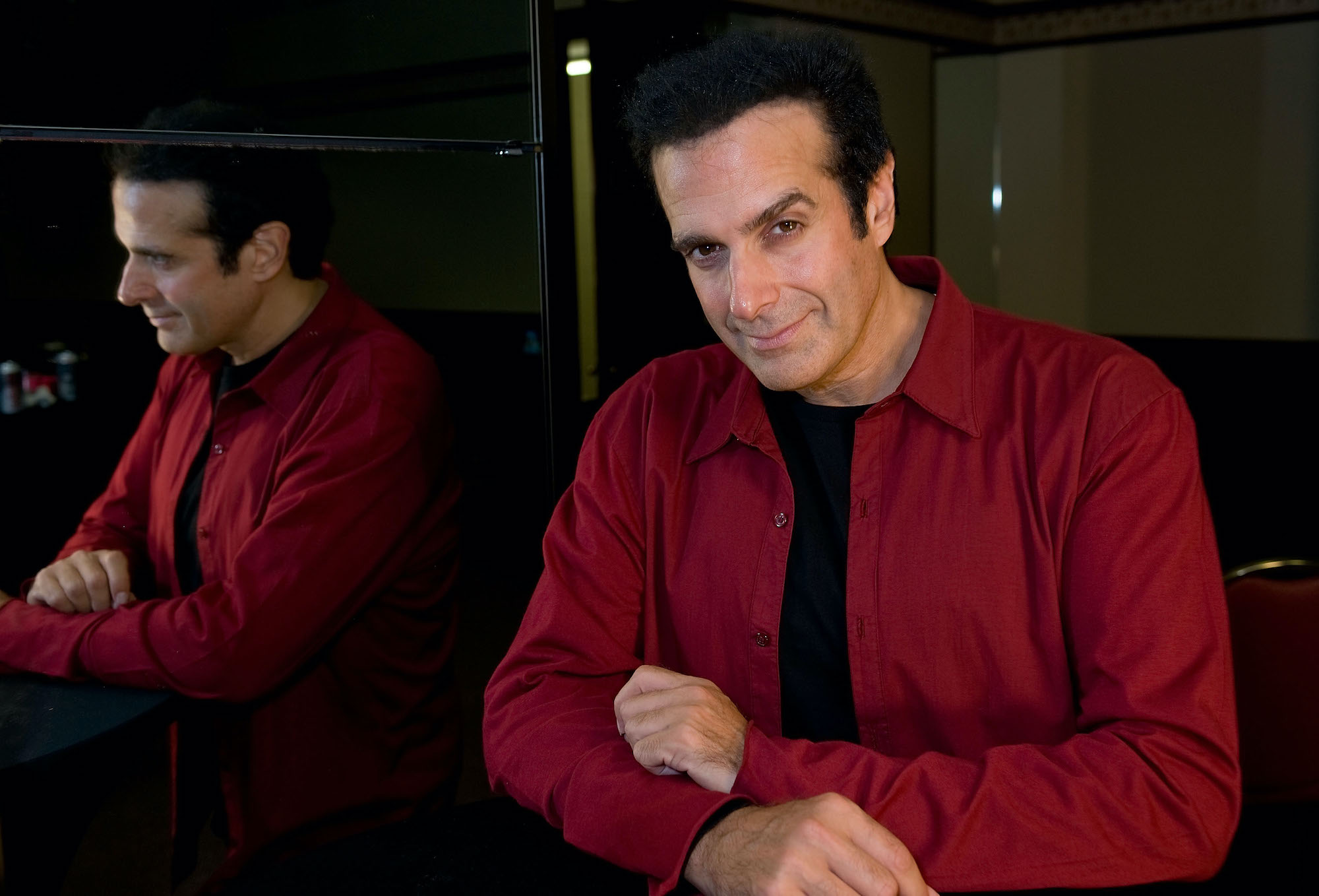 David Copperfield smiling at the camera to the right of a mirror