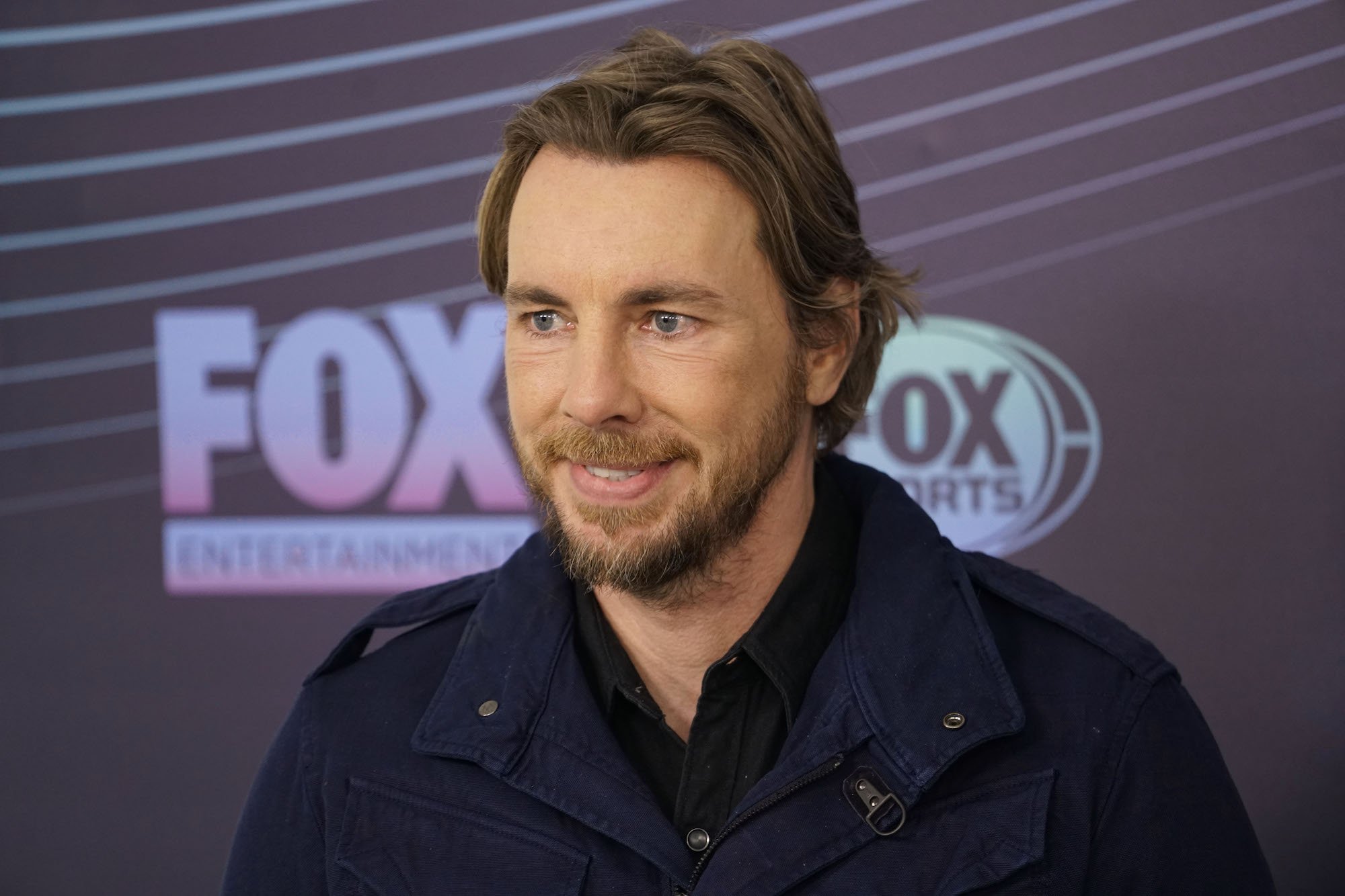 Dax Shepard smiling in front of a dark background