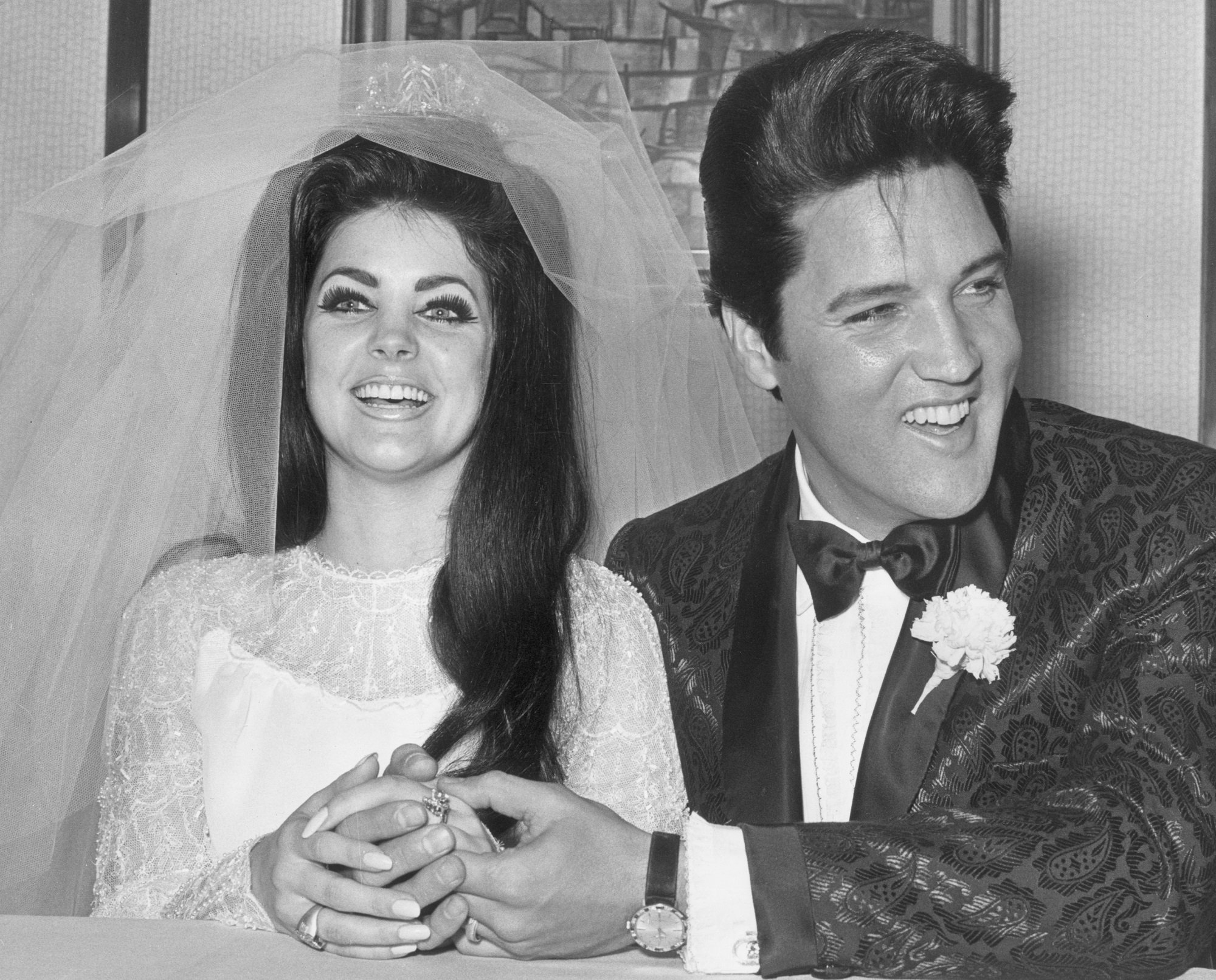 A black-and-white photo of Elvis Presley holding hands with Priscilla Beaulieu Presley on their wedding day