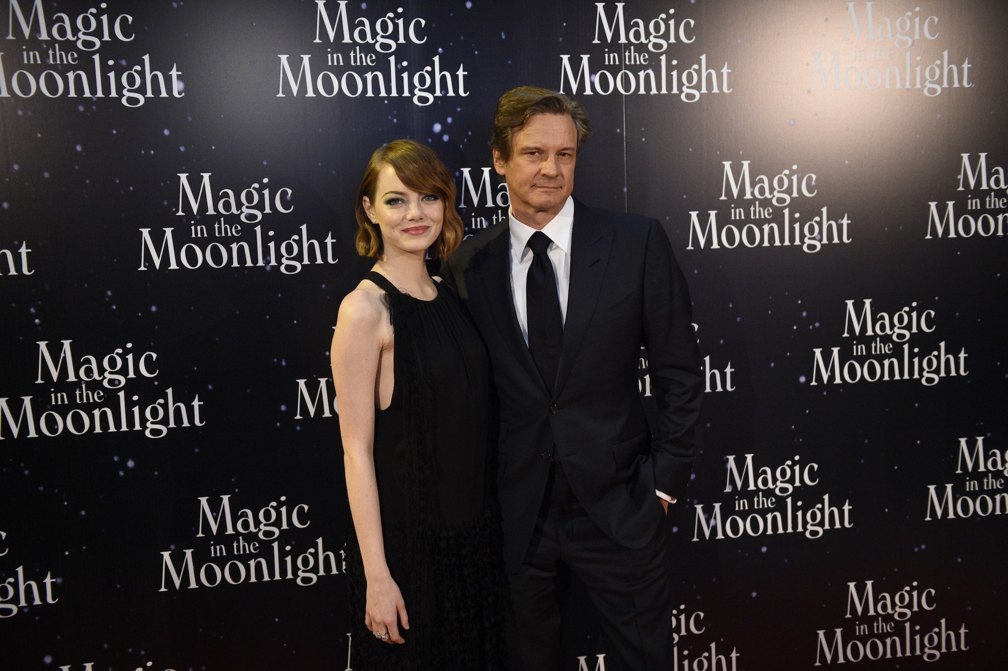 (L-R) Emma Stone and Colin Firth smiling in front of a black background with repeating logos