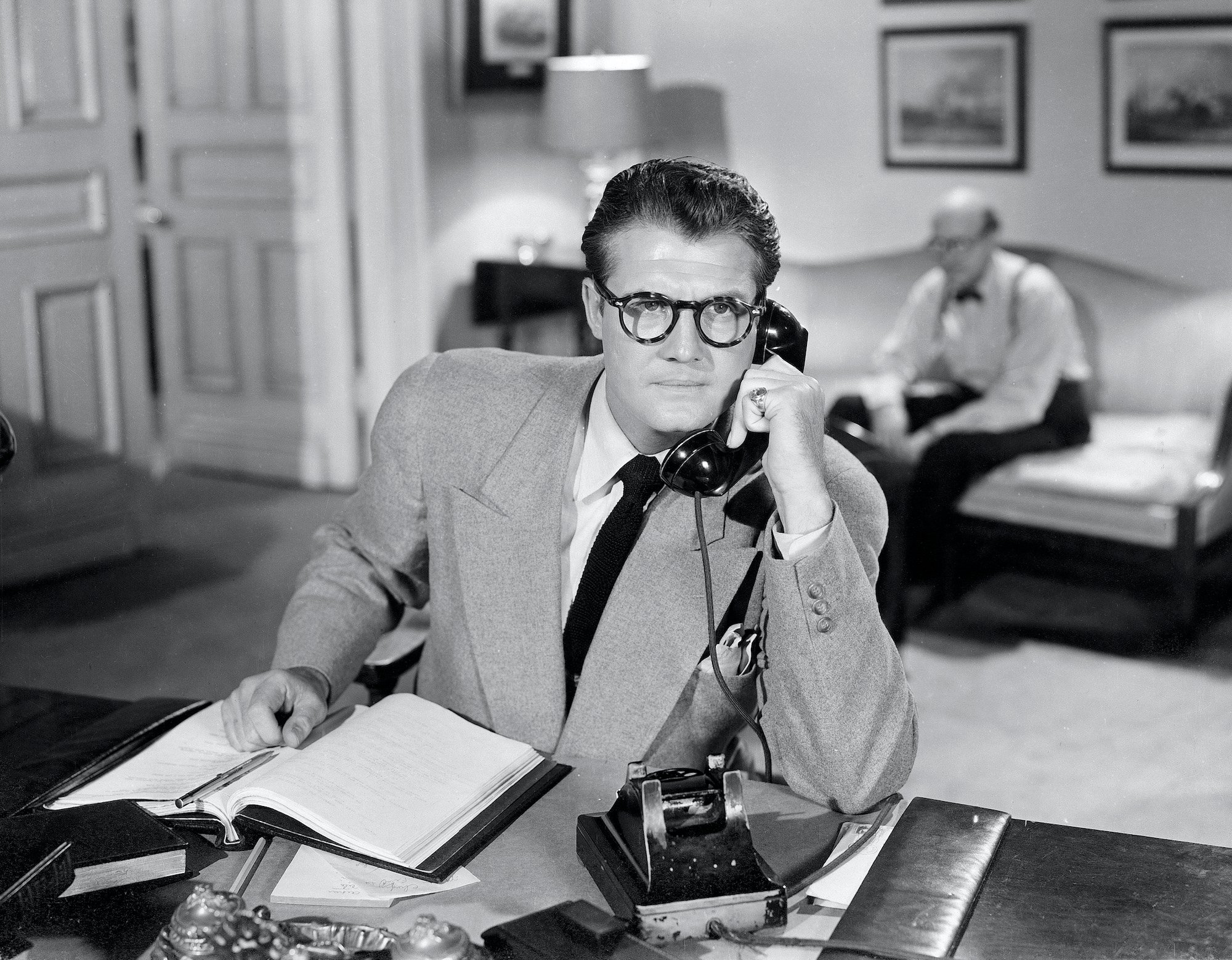 George Reeves as Clark Kent in 'The Adventures of Superman', posed using a phone, in black and white