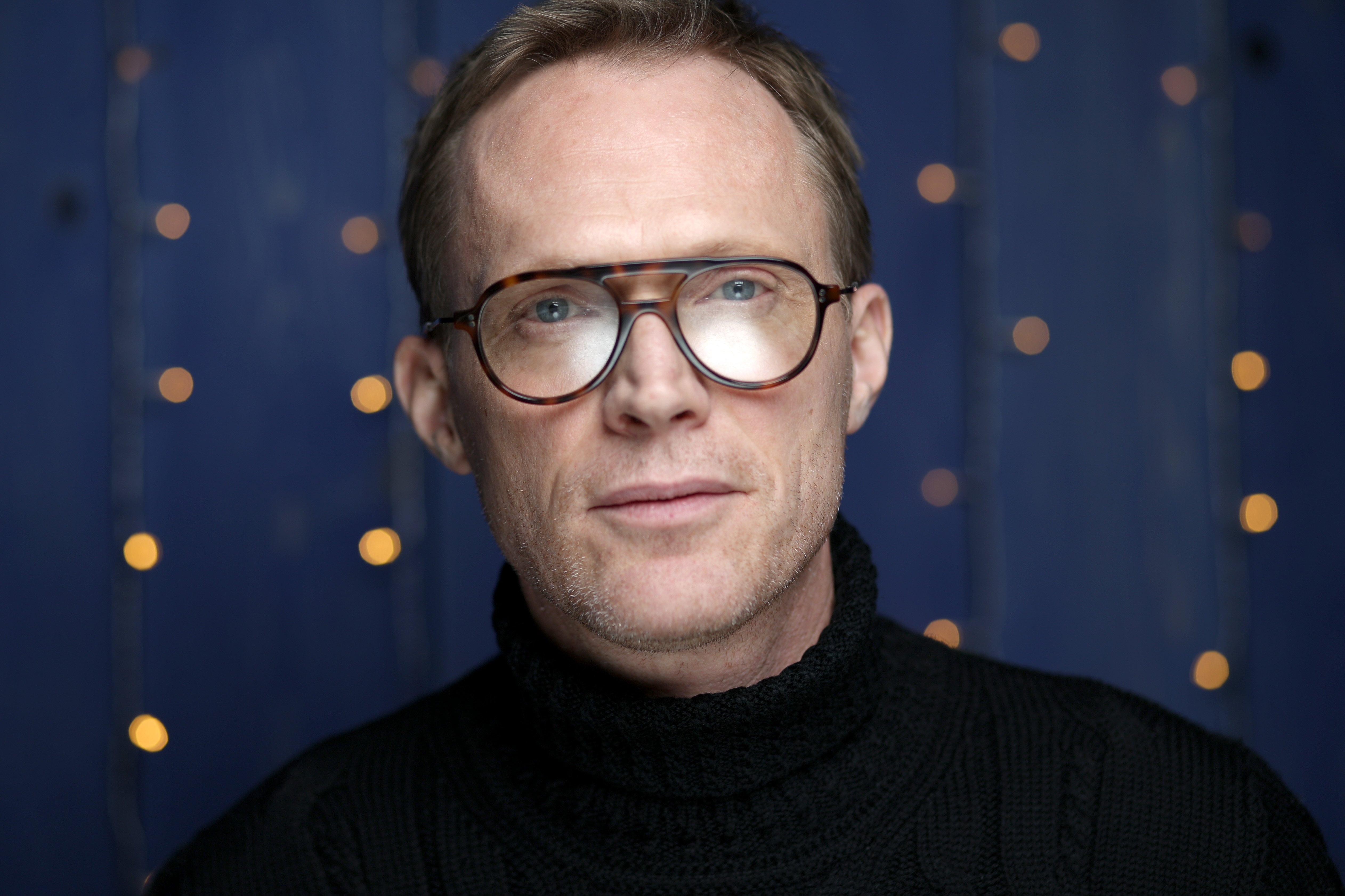 headshot of Paul Bettany wearing glasses and a black shirt