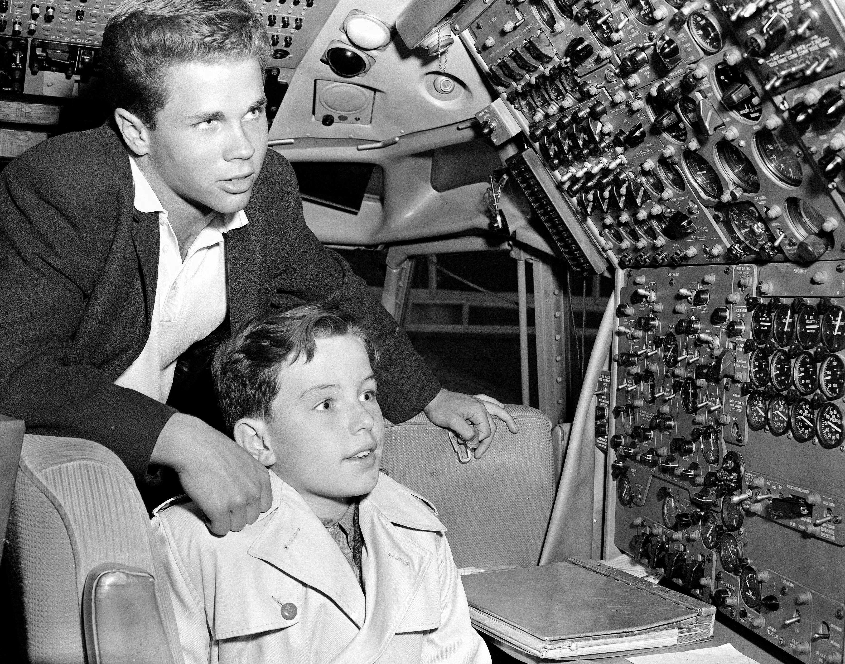 Tony Dow stands behind Jerry Mathers as he sits in a chair in the cockpit of an airplane