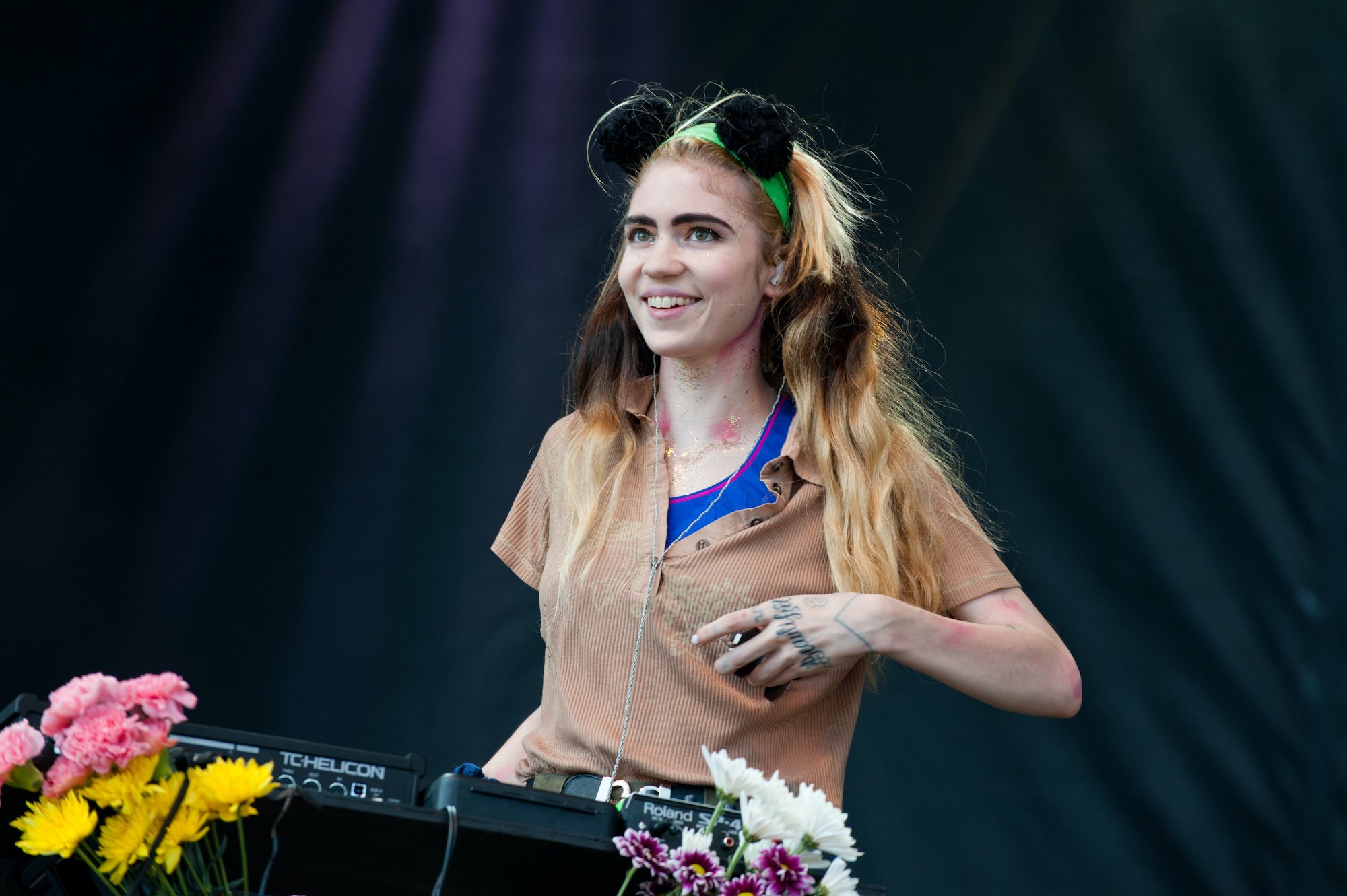 Grimes smiling, behind a keyboard and flowers, in front of a black curtain, on stage