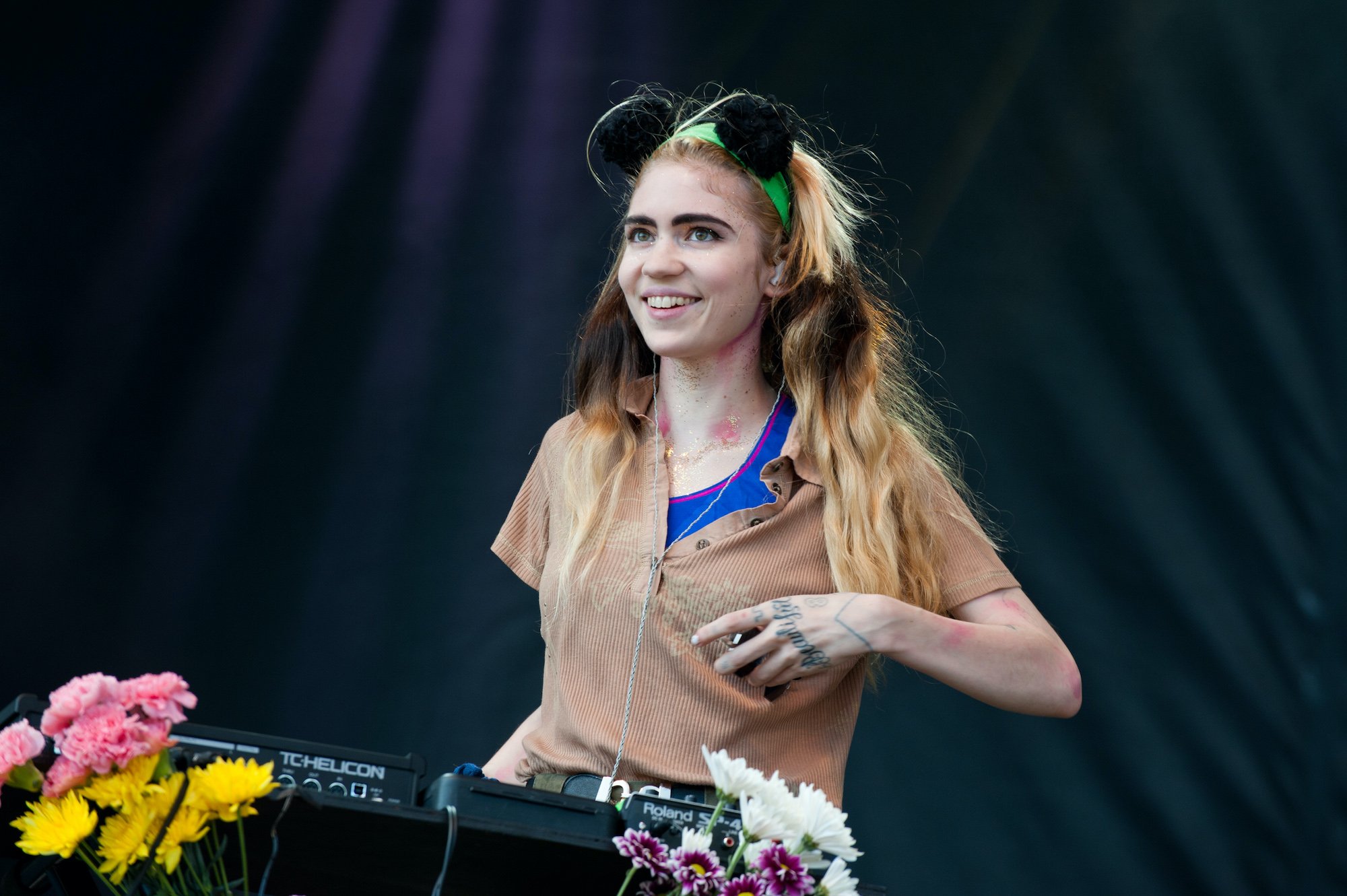 Grimes smiling, behind a keyboard and flowers, in front of a black curtain, on stage