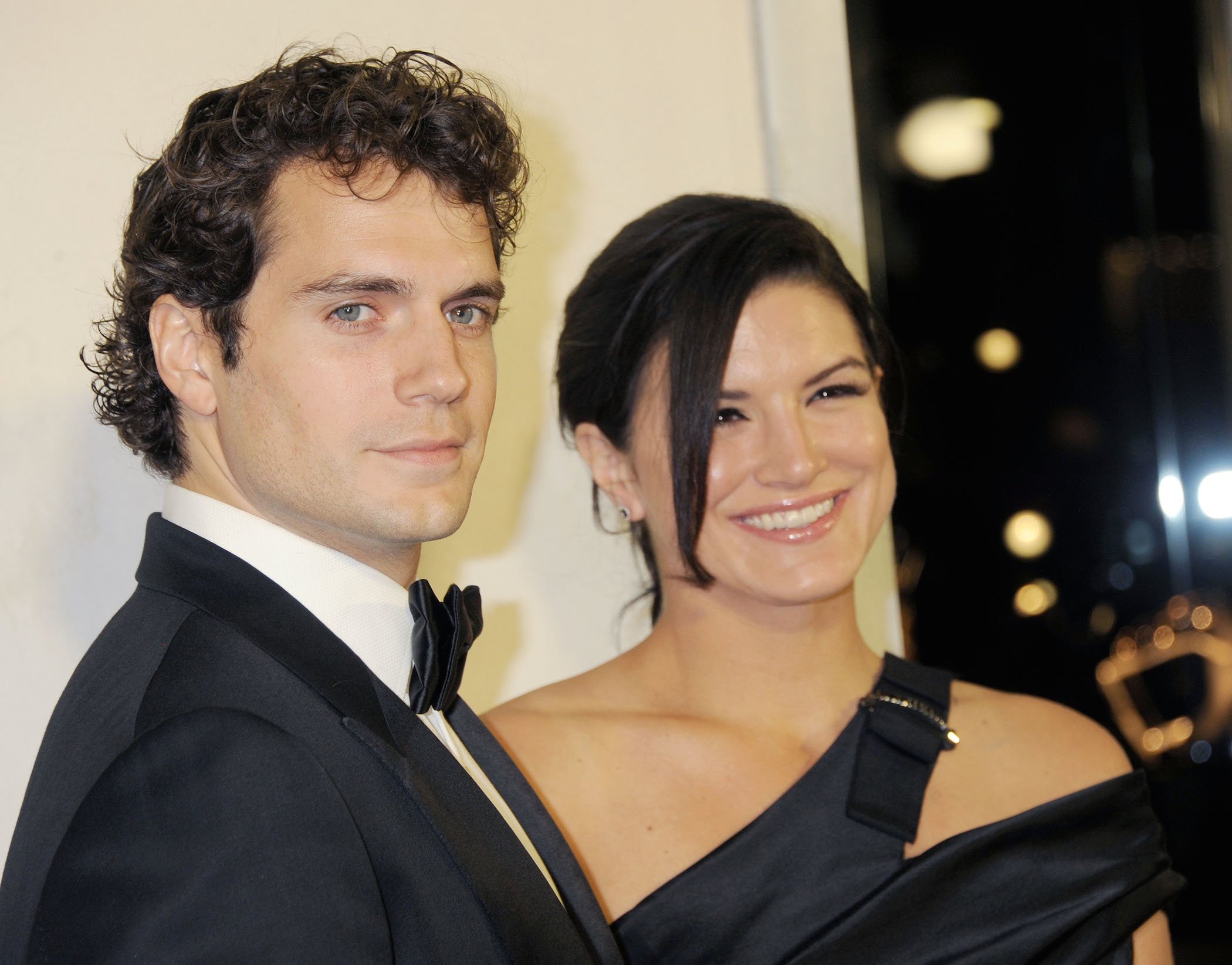 Henry Cavill and Gina Carano smiling together at a cocktail party