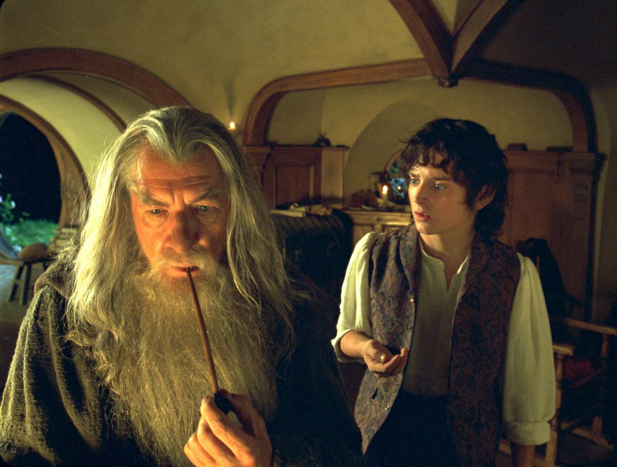 Ian McKellen as Gandalf standing in the front with a pipe in his hand, with Elijah Wood as Frodo standing behind him.
