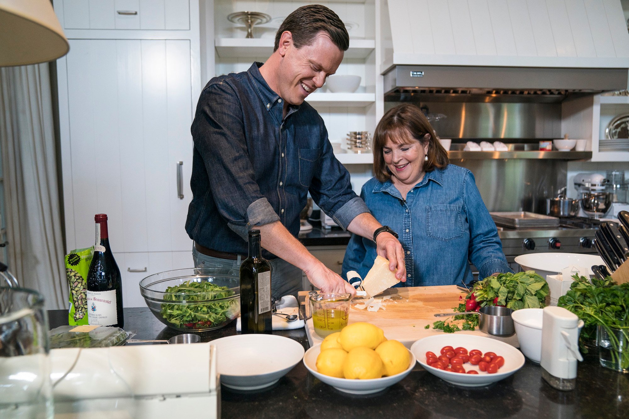 (L-R) Willie Geist and Ina Garten in a kitchen, laughing and preparing a meal