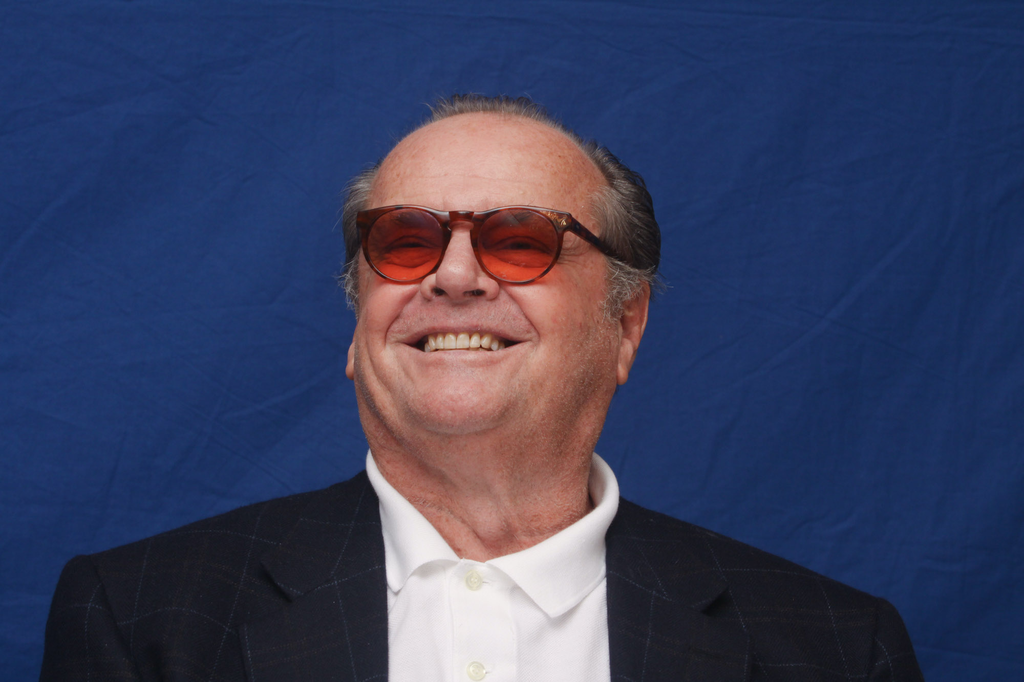 Jack Nicholson smiling in front of a blue backdrop, wearing sunglasses