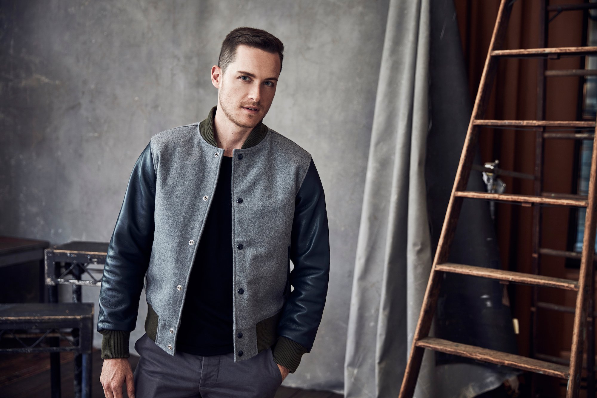 Jesse Lee Soffer posing in front of a gray curtain and a wooden ladder