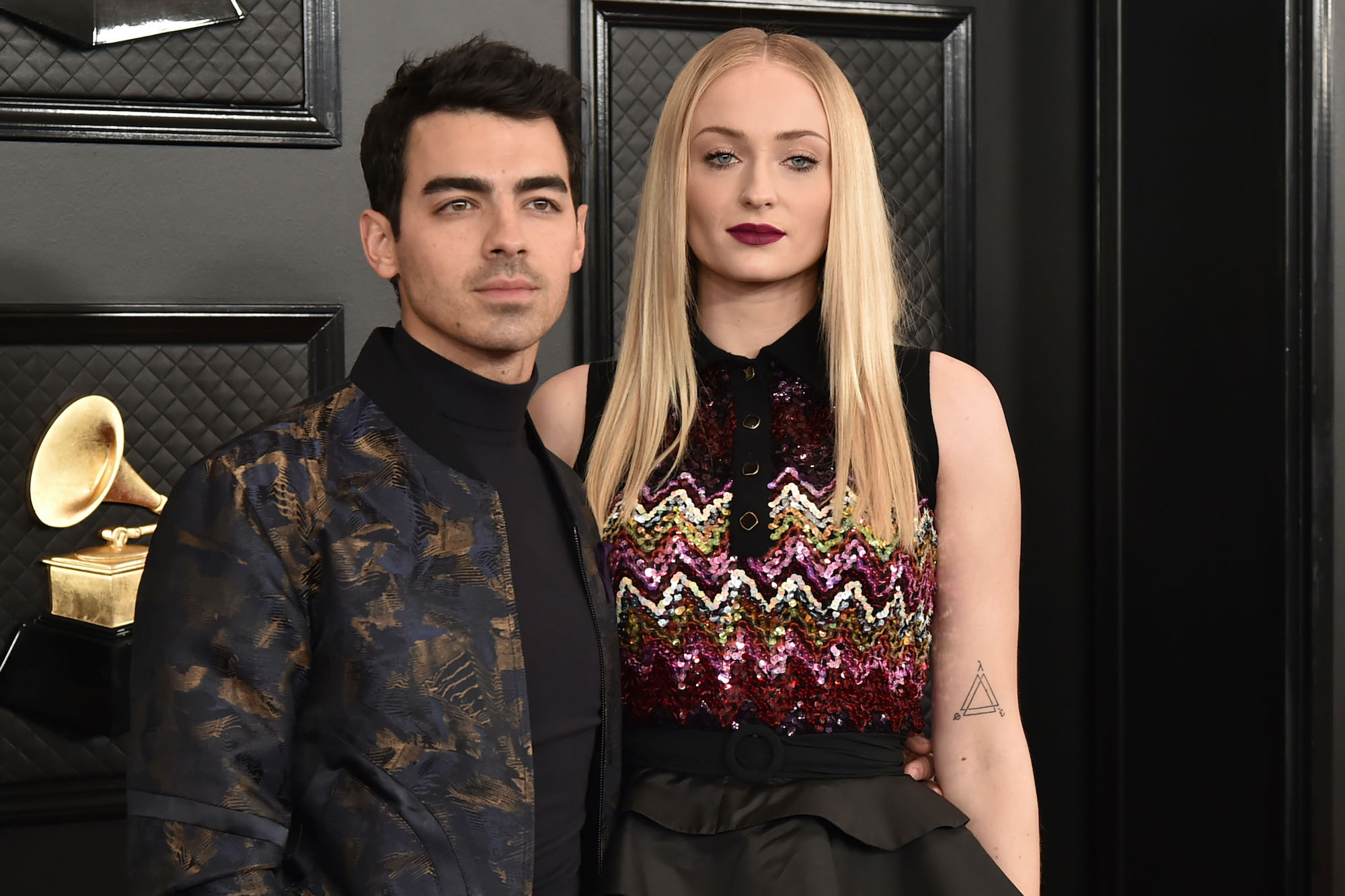 (L-R) Joe Jonas and Sophie Turner standing in front of a black background