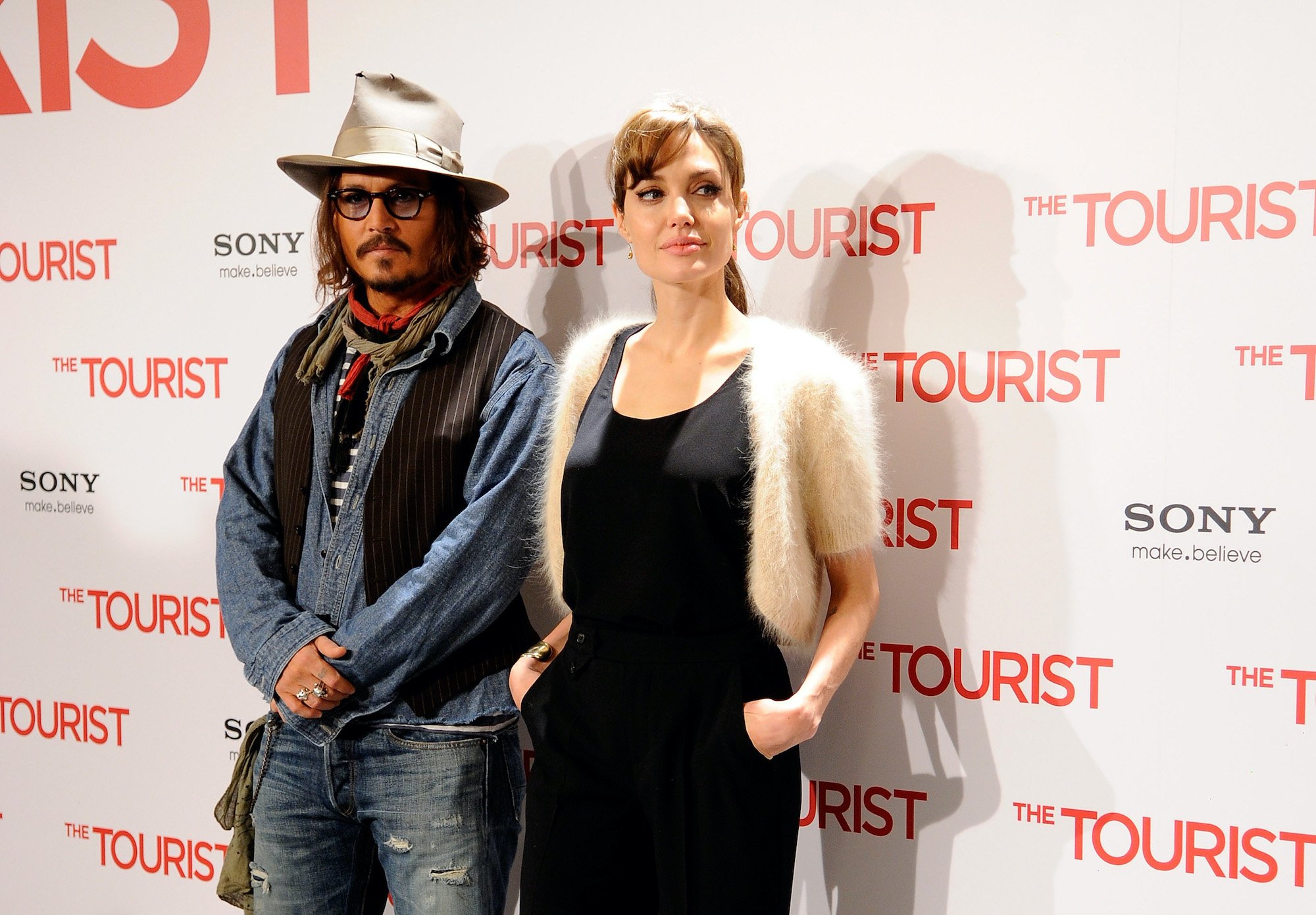 (L-R) Johnny Depp and Angelina Jolie smiling in front of a while background with repeating logos
