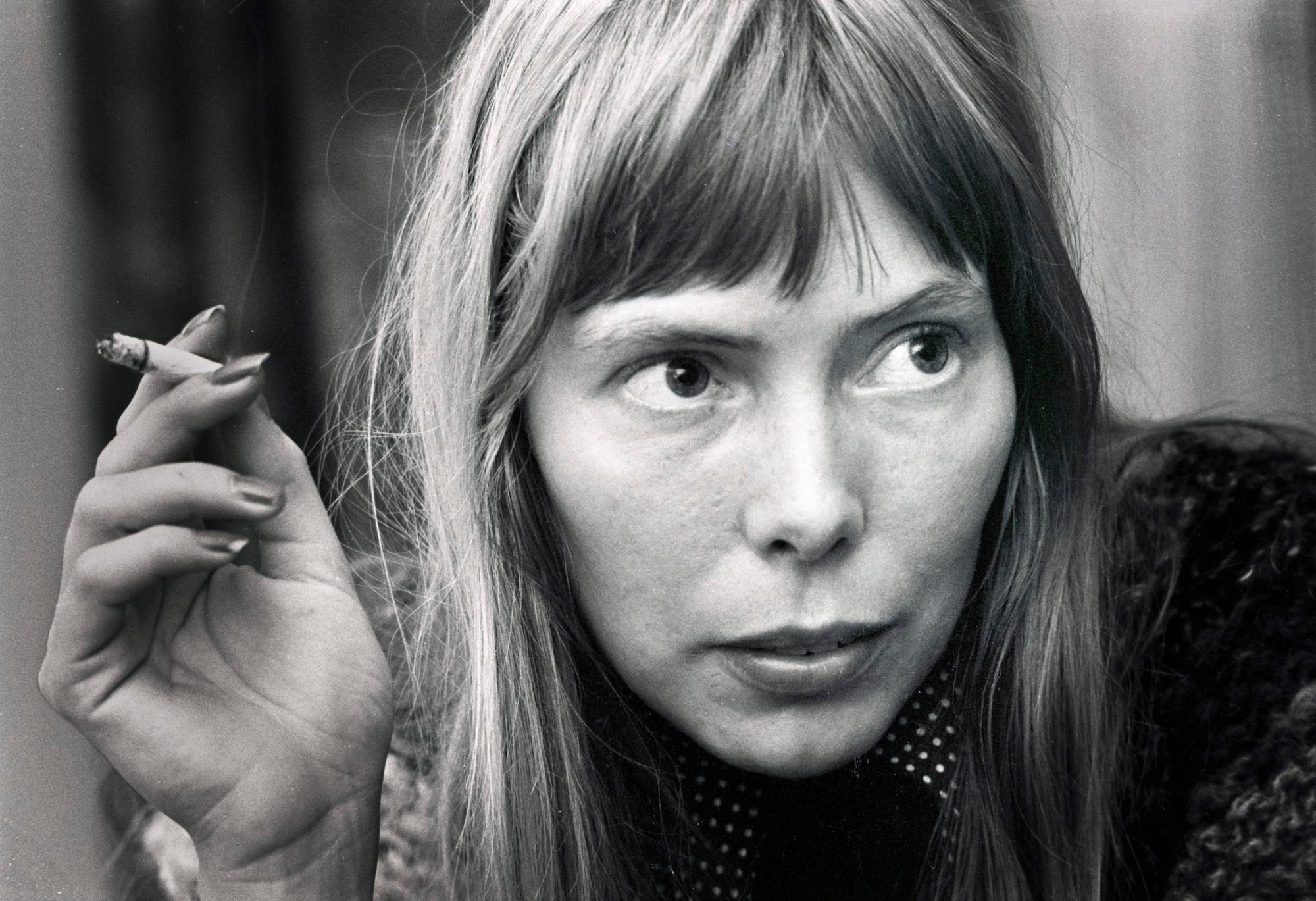 Joni Mitchell looking off to the right, holding a cigarette, in black and white