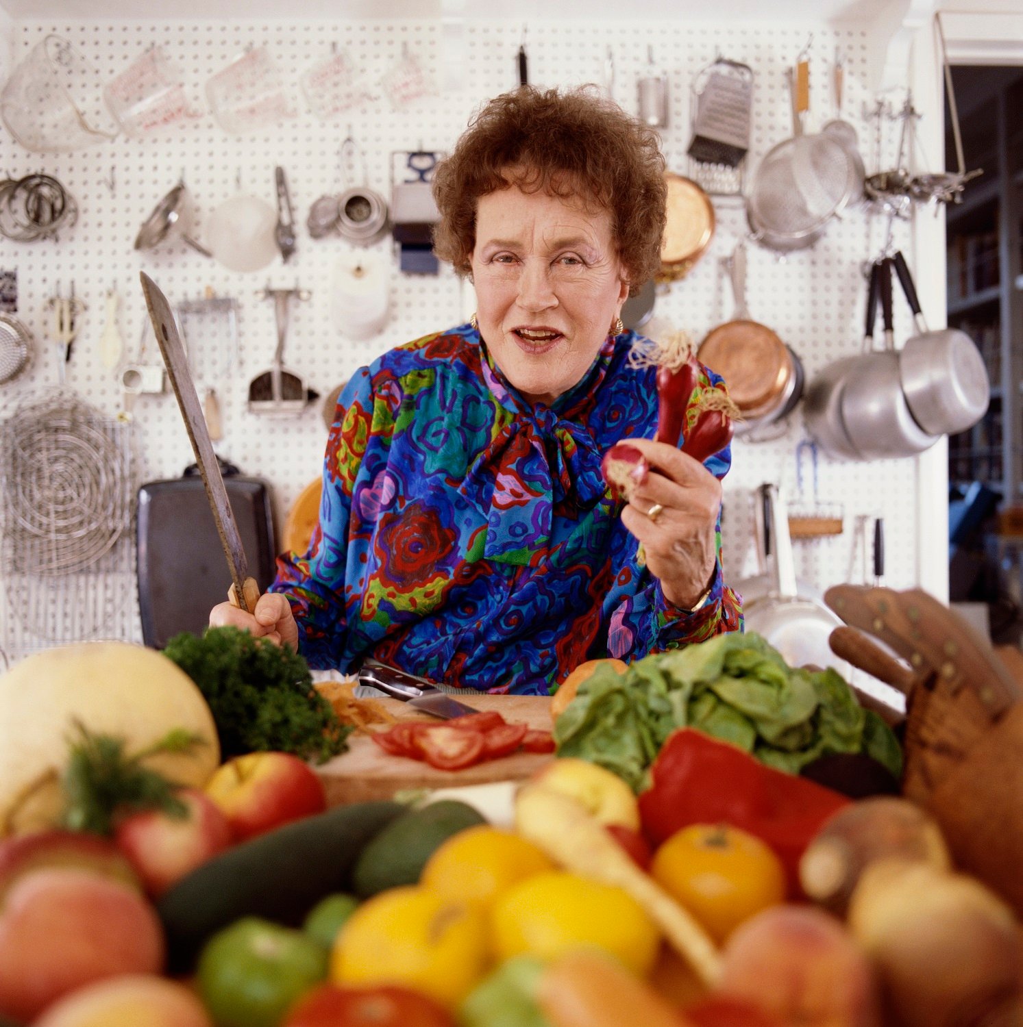 Julia Child photographed posing in her kitchen chopping vegetables