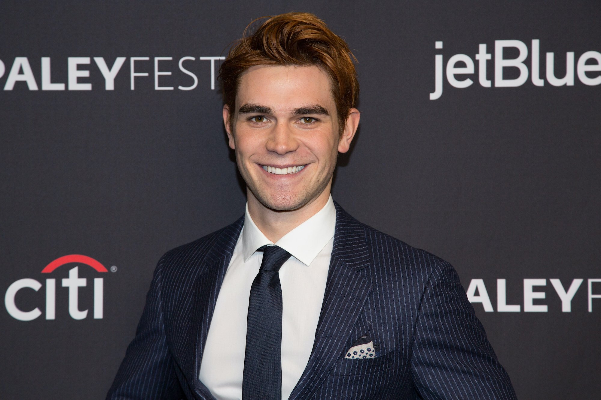 K.J. Apa smiling in front of a black background