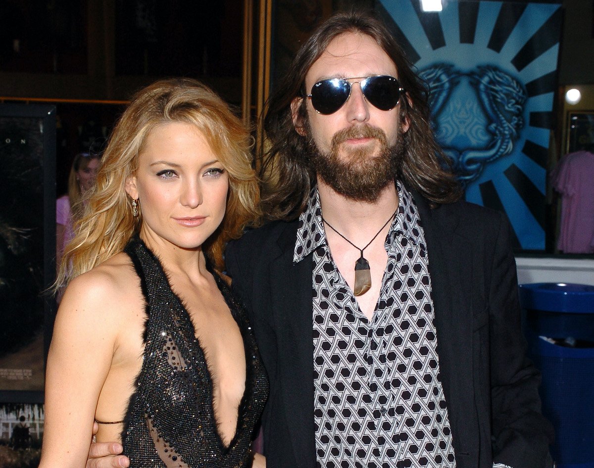 Kate Hudson in a black sleeveless dress poses with husband Chris Robinson, wearing jeans, a patterned shirt, and black blazer with sunglasses | SGranitz/WireImage
