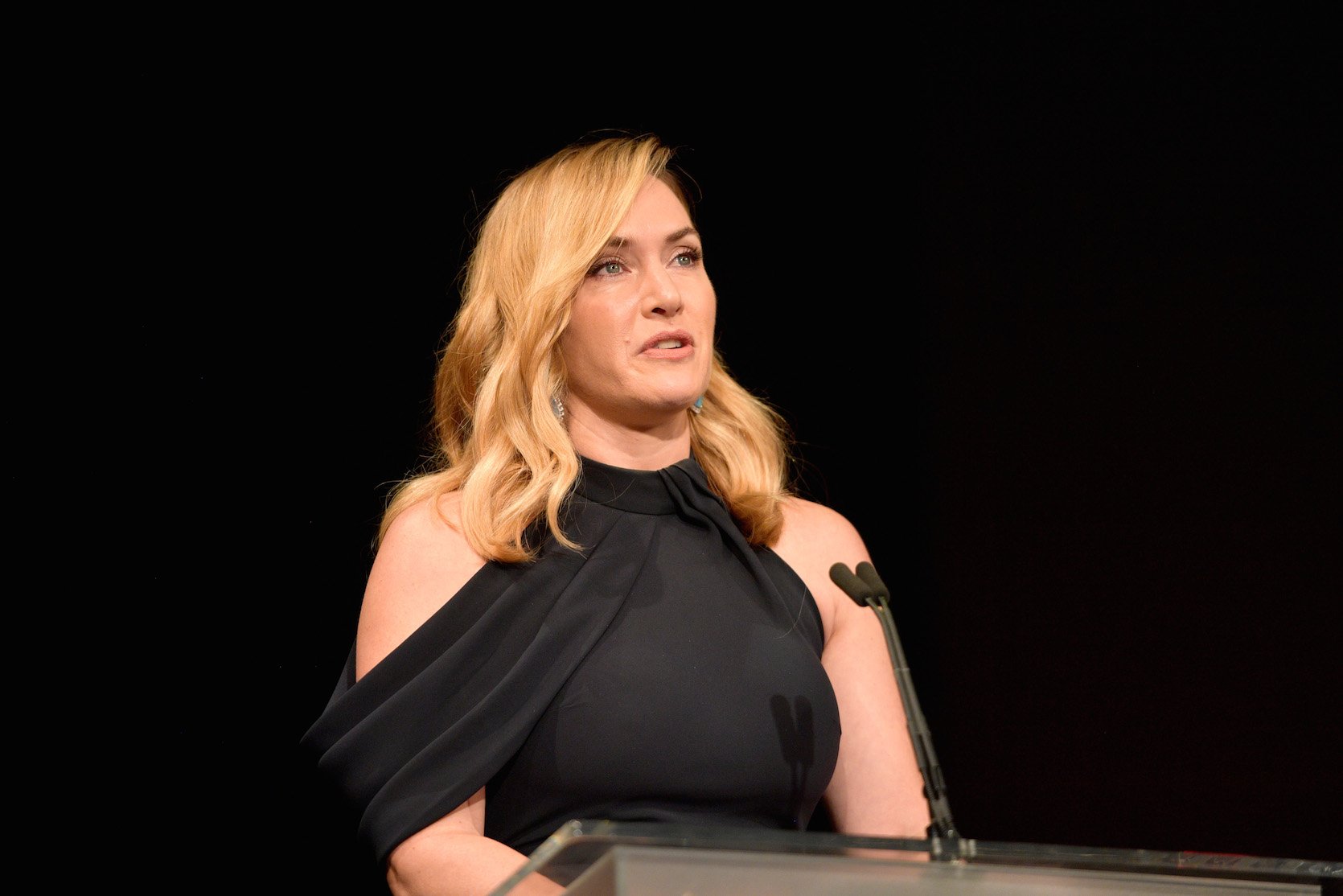 Kate Winslet in a black dress accepting an award at a podium