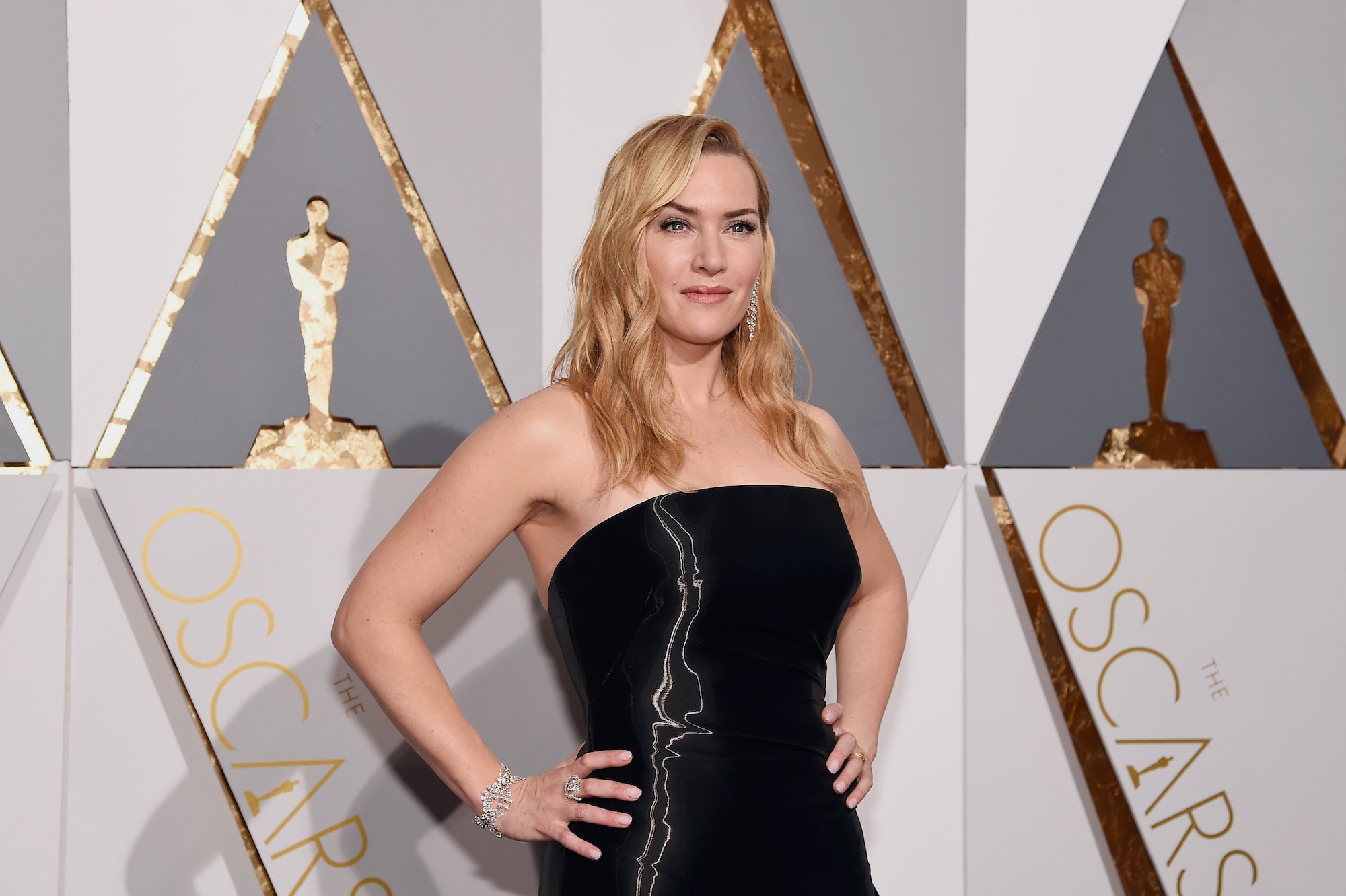 Kate Winslet smiling in front of a gray, white, and gold background