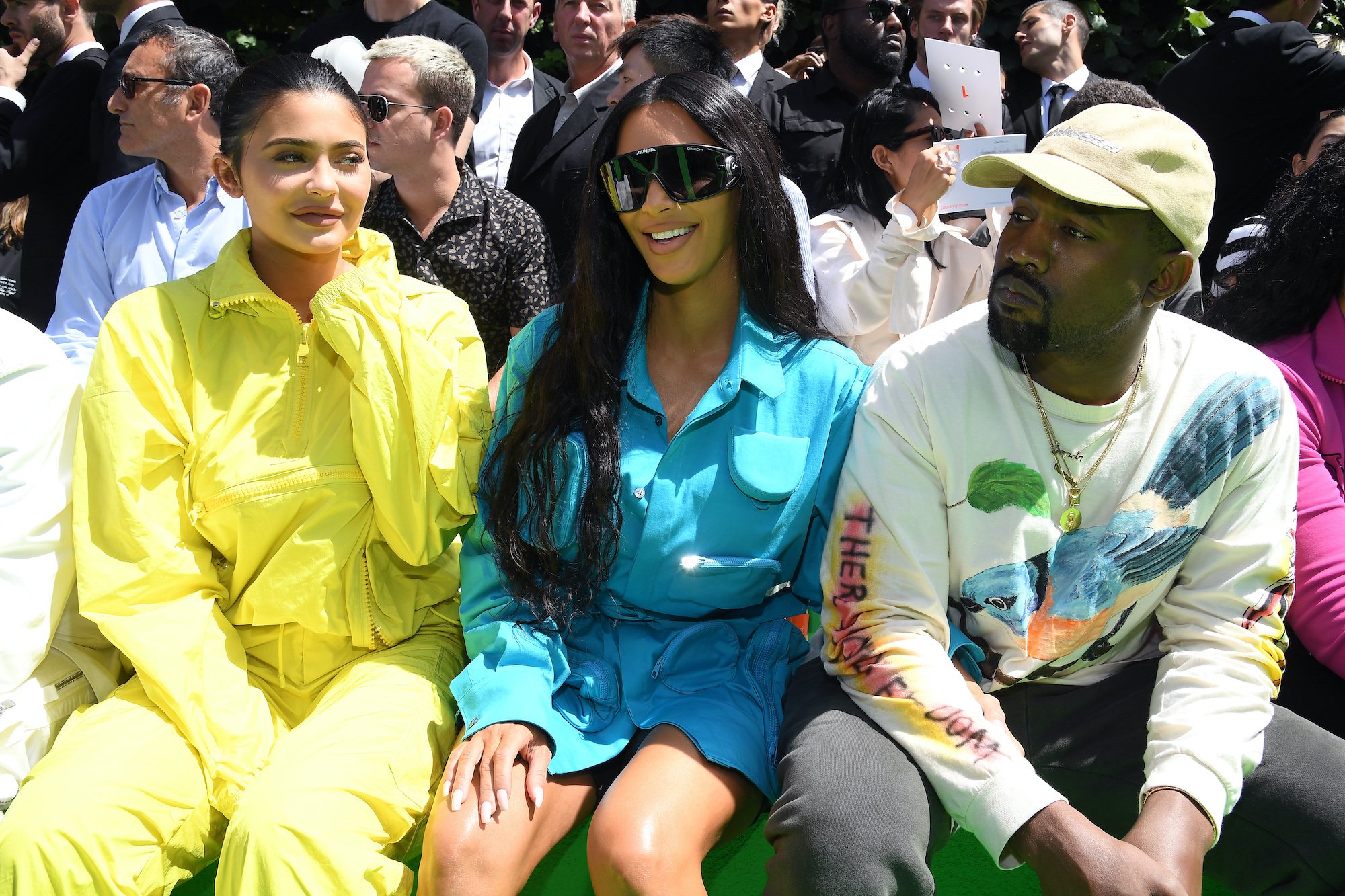 (L-R) Kylie Jenner, Kim Kardashian West, and Kanye West sitting at a fashion show in front of a crowd