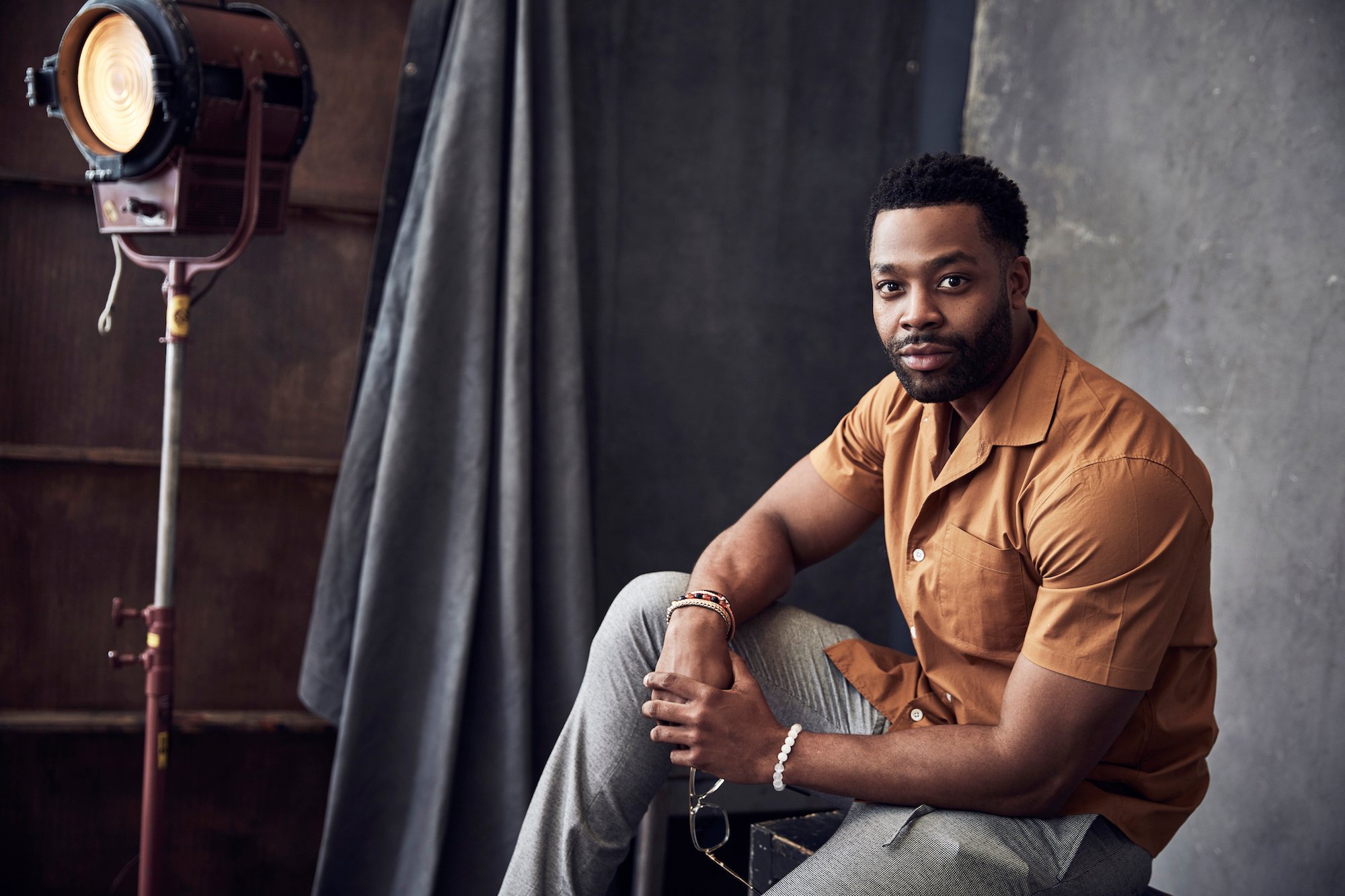 LaRoyce Hawkins smiling, posed on a block in front of a gray background and vintage photography light