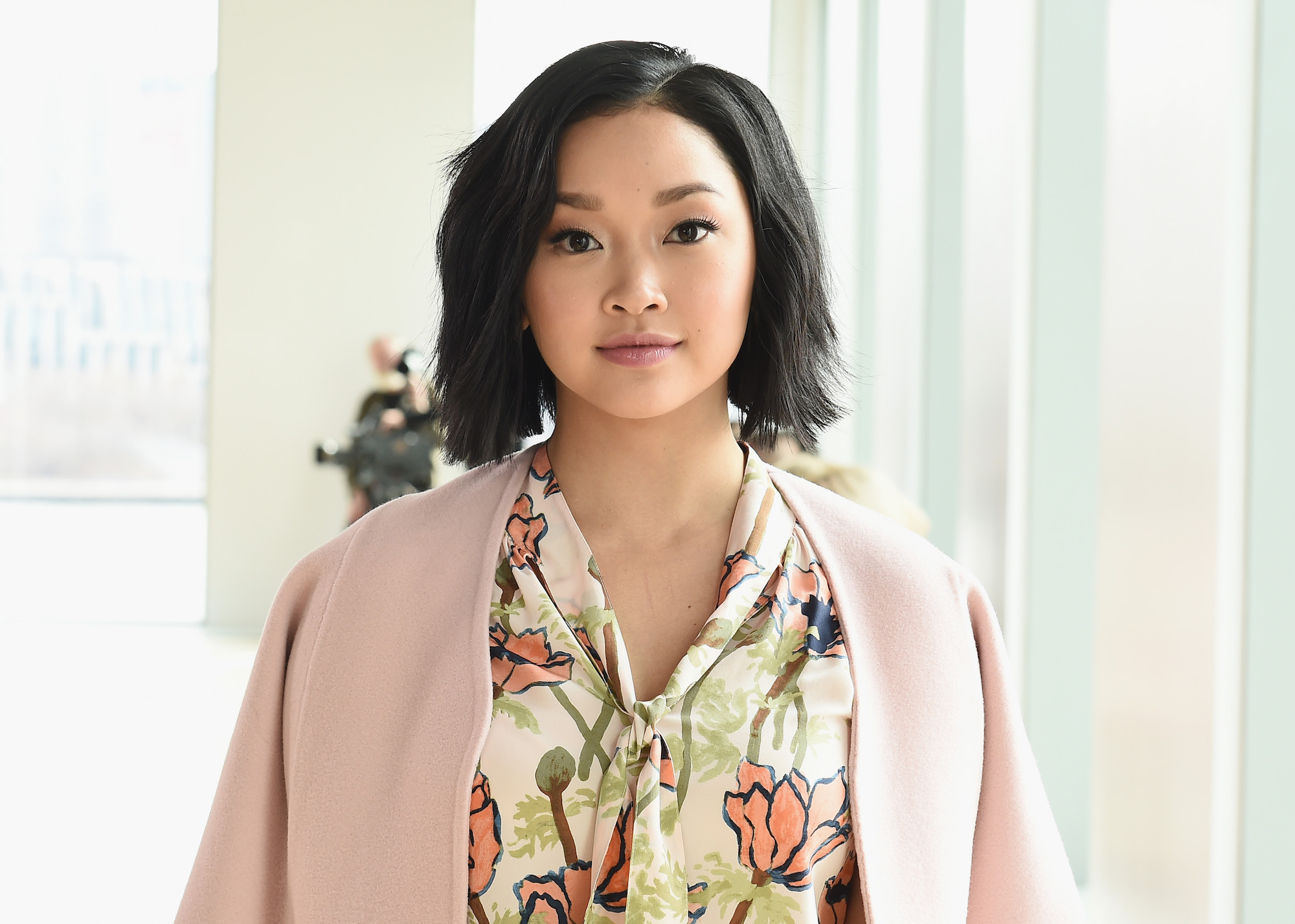 Lana Condor smiling at the camera, in front of a blurred white background