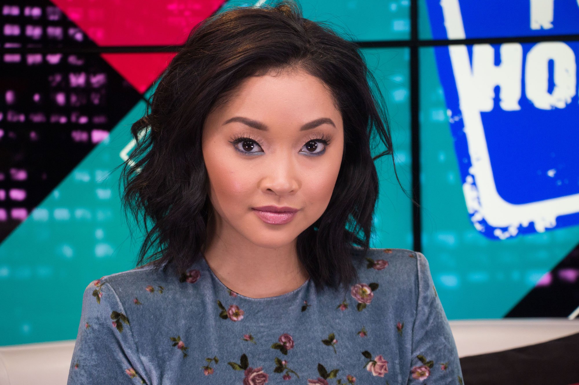 Lana Condor smiling at the camera, in front of a multicolor background