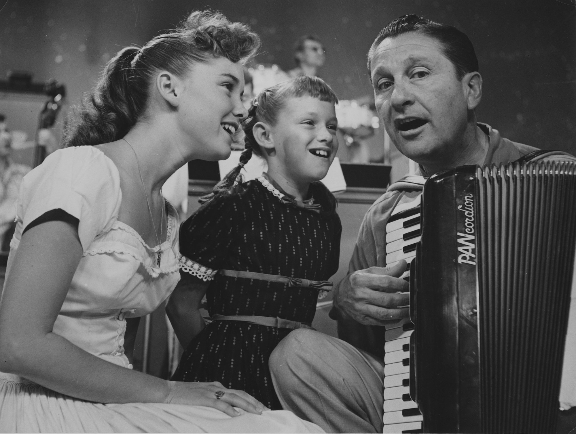 (L-R) Dianne Lennon, Janet Lennon, and Lawrence Welk playing an accordion, in black and white