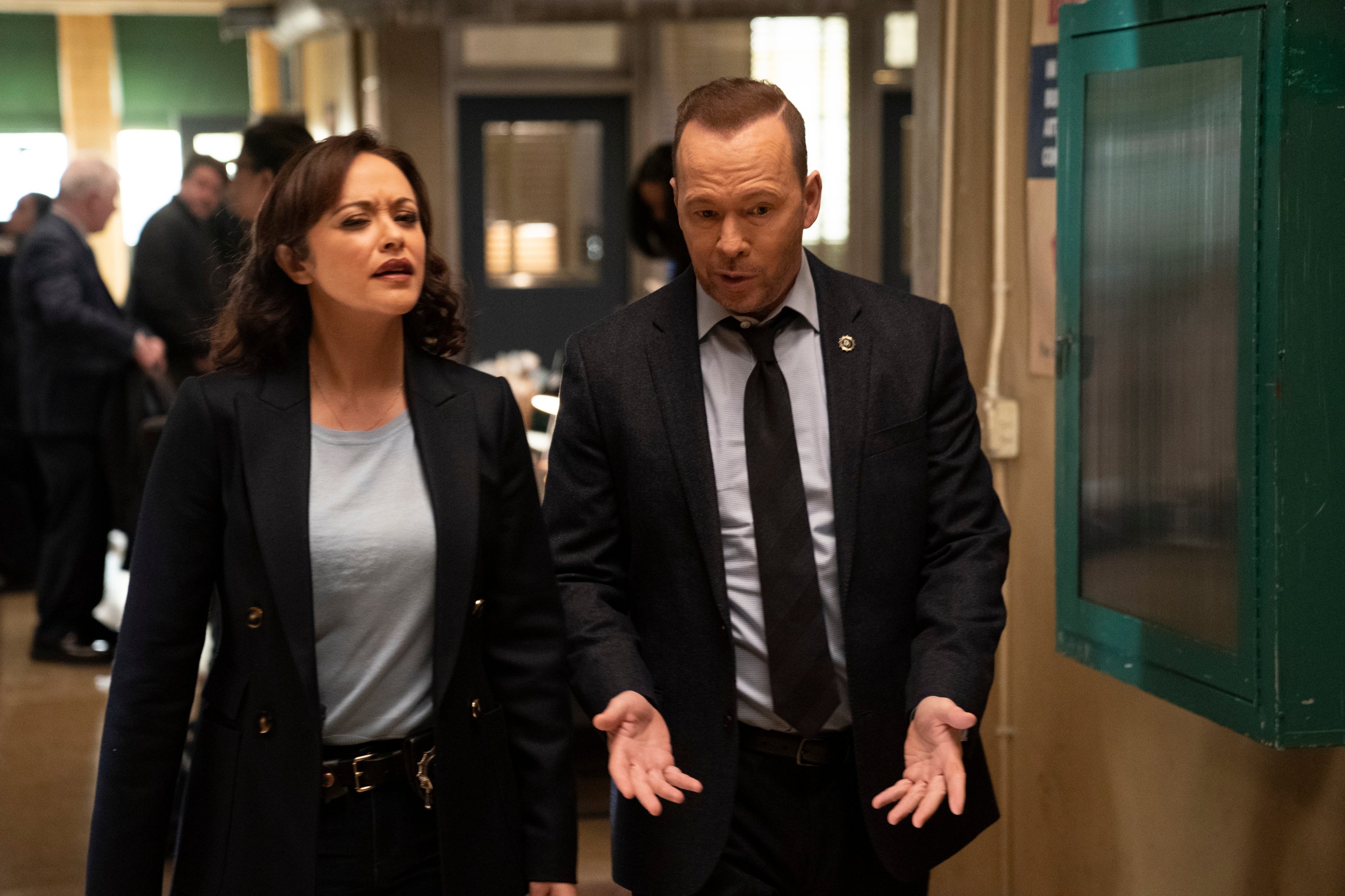 Marisa Ramirez and Donnie Wahlberg walk next to each other talking in a hallway on the set of 'Blue Bloods'
