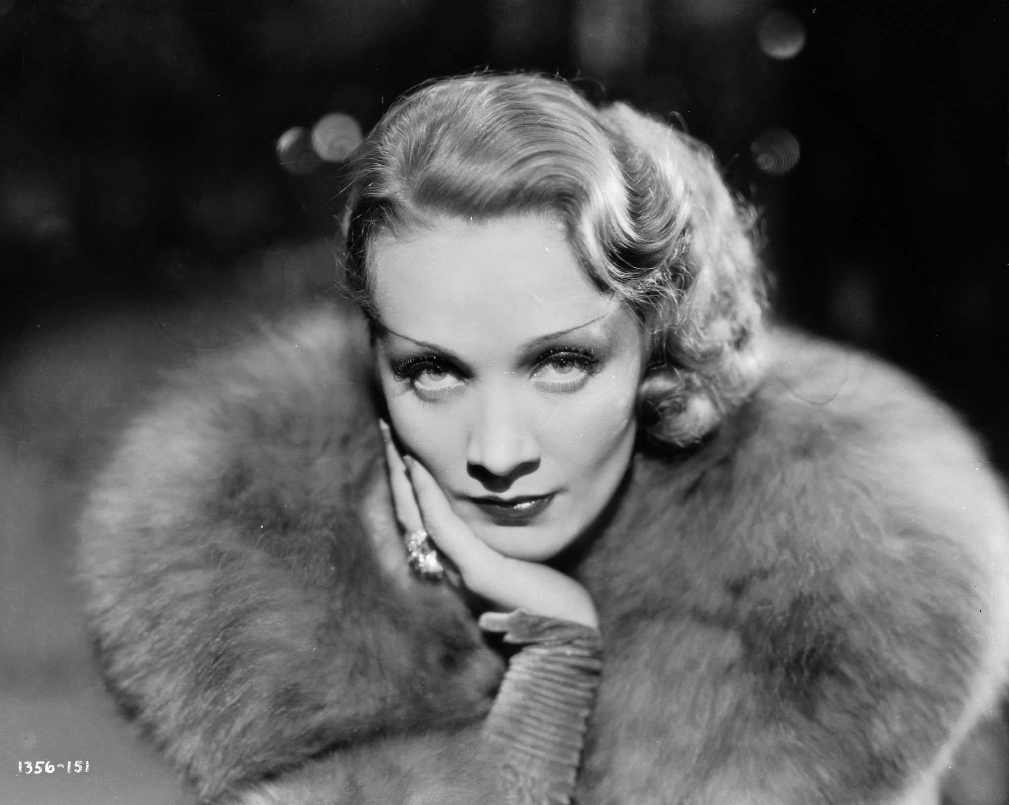 Marlene Dietrich looking up at the camera with a large fur collar, in black and white