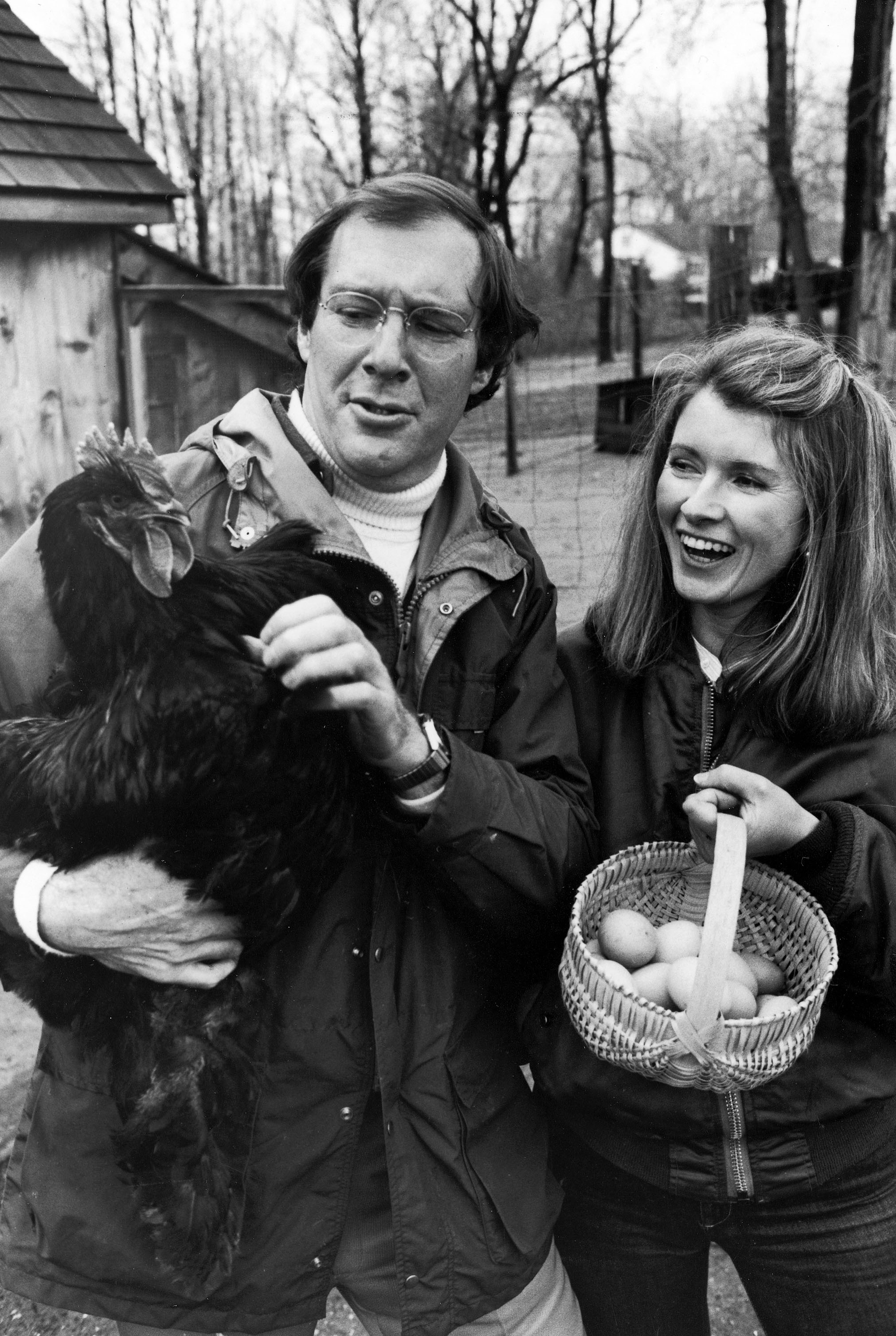 Andy Stewart holding a black Cochin hen and wife, Martha Stewart, holding a basket of eggs in barnyard